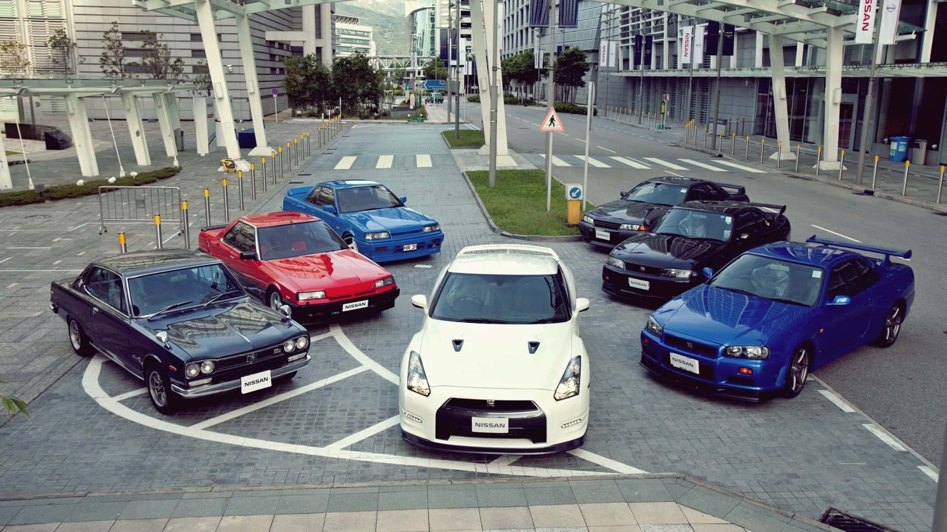 R33 GT-R 桌布 壁紙 — 從高角度俯瞰七輛經典和現代日產跑車以幾何圖案停放在城市廣場上。