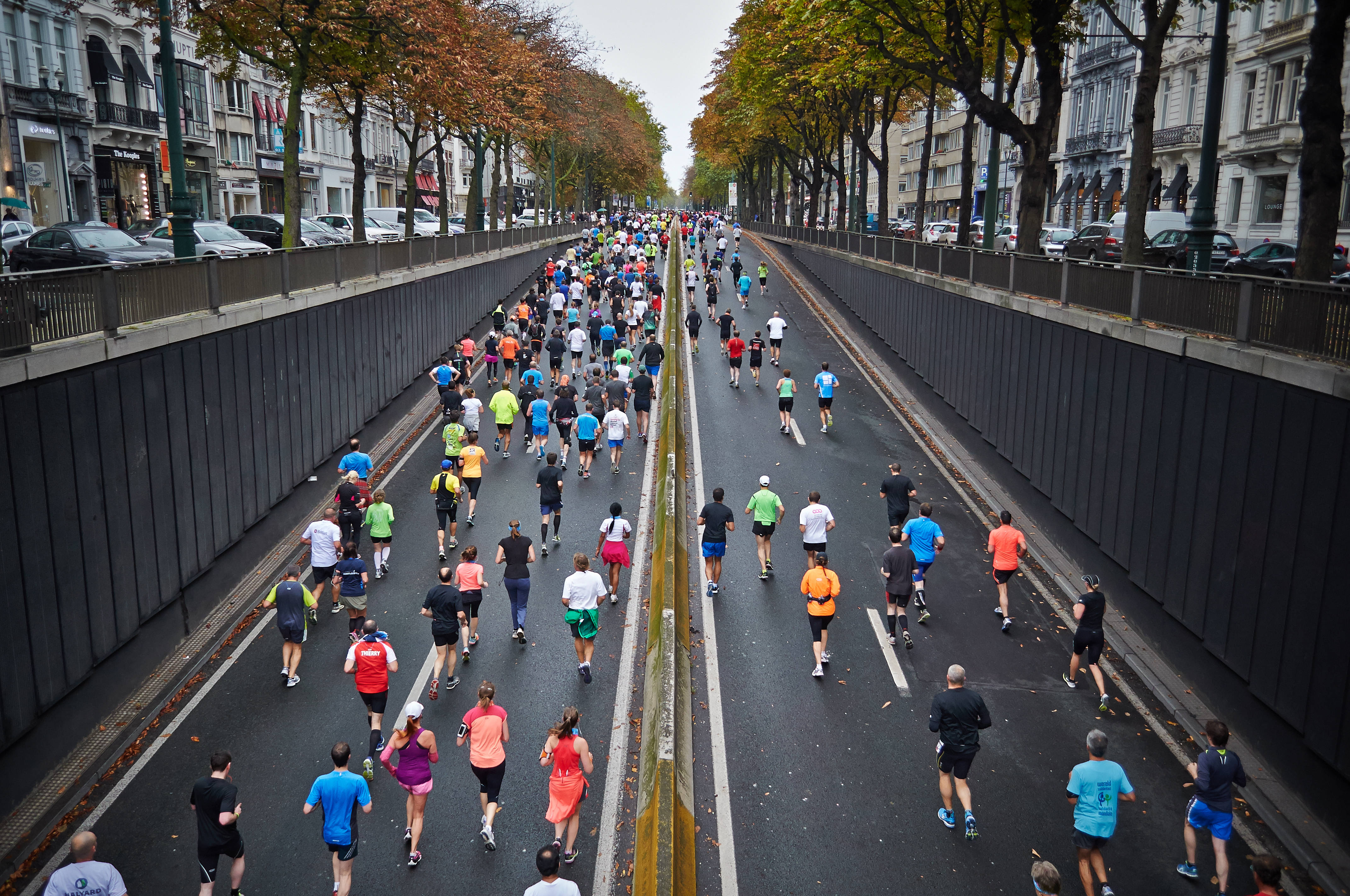 Marathon 桌布 壁紙 — 從高角度俯瞰數百名身穿色彩繽紛運動裝備的跑者，在兩旁種滿樹木、歷史建築和秋葉的都市大道上衝刺。