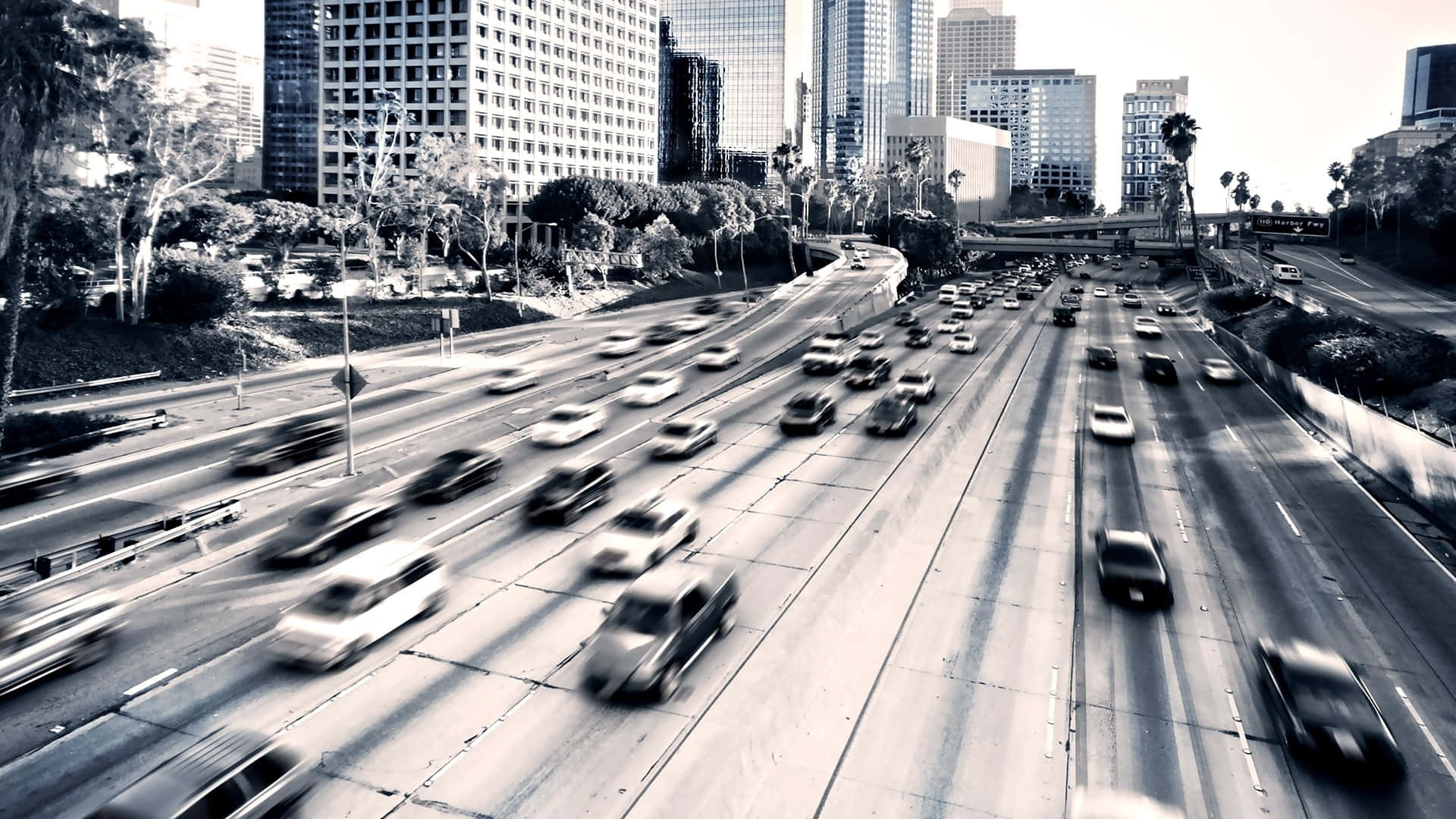 La 桌布 壁紙 — 從高角度俯瞰繁忙的城市高速公路，車流在摩天大樓下流動，呈現動態模糊效果。