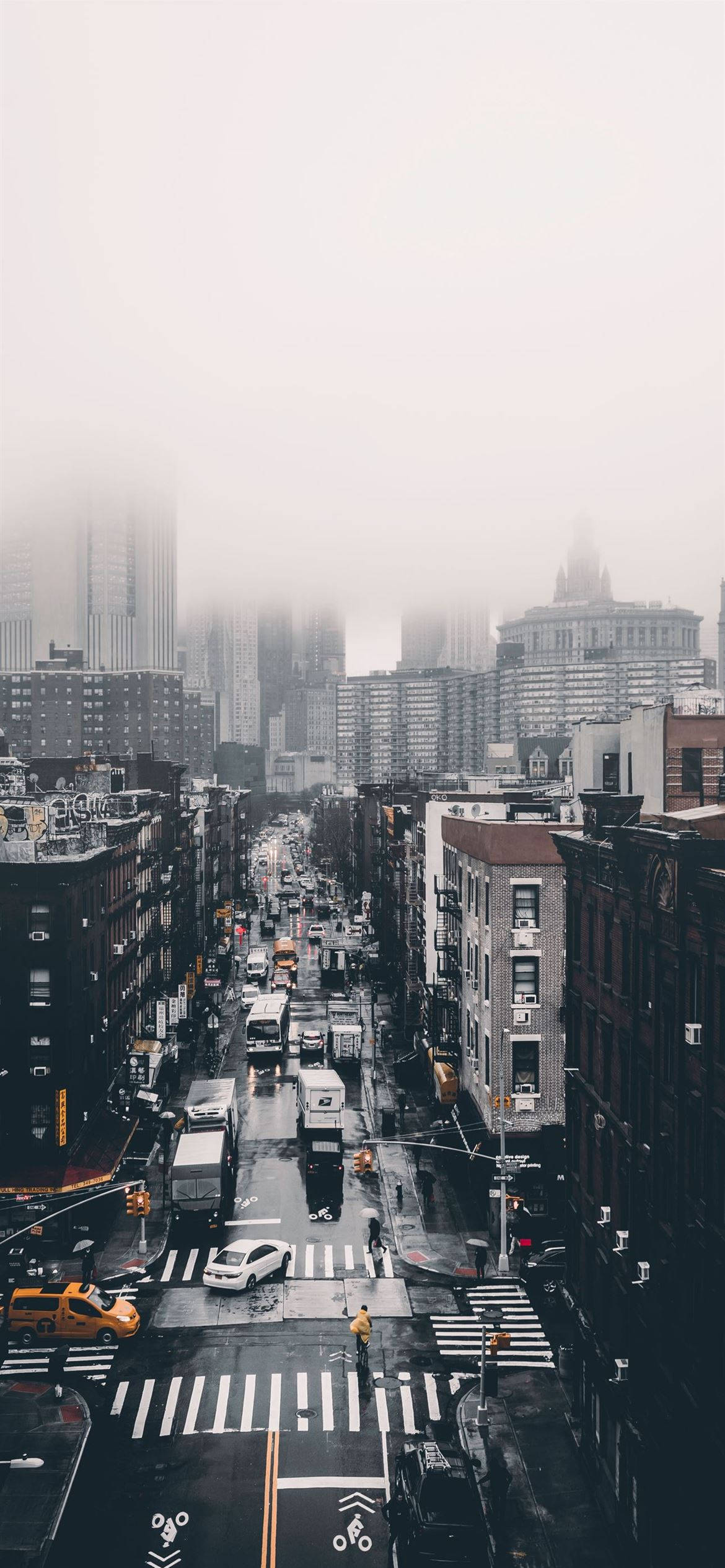 City Street 桌布 壁紙 — 從高角度俯瞰霧氣瀰漫的城市街道，濕漉漉的路面反射著柔和的城市燈光，遠方的高樓大廈模糊不清。