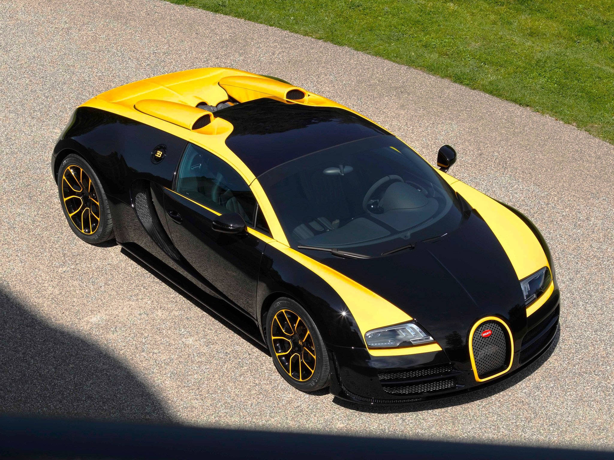 Cool Bugatti 桌布 壁紙 — 從高角度拍攝一輛黑黃色Bugatti Veyron停泊在碎石車道上，旁邊有綠色草地。