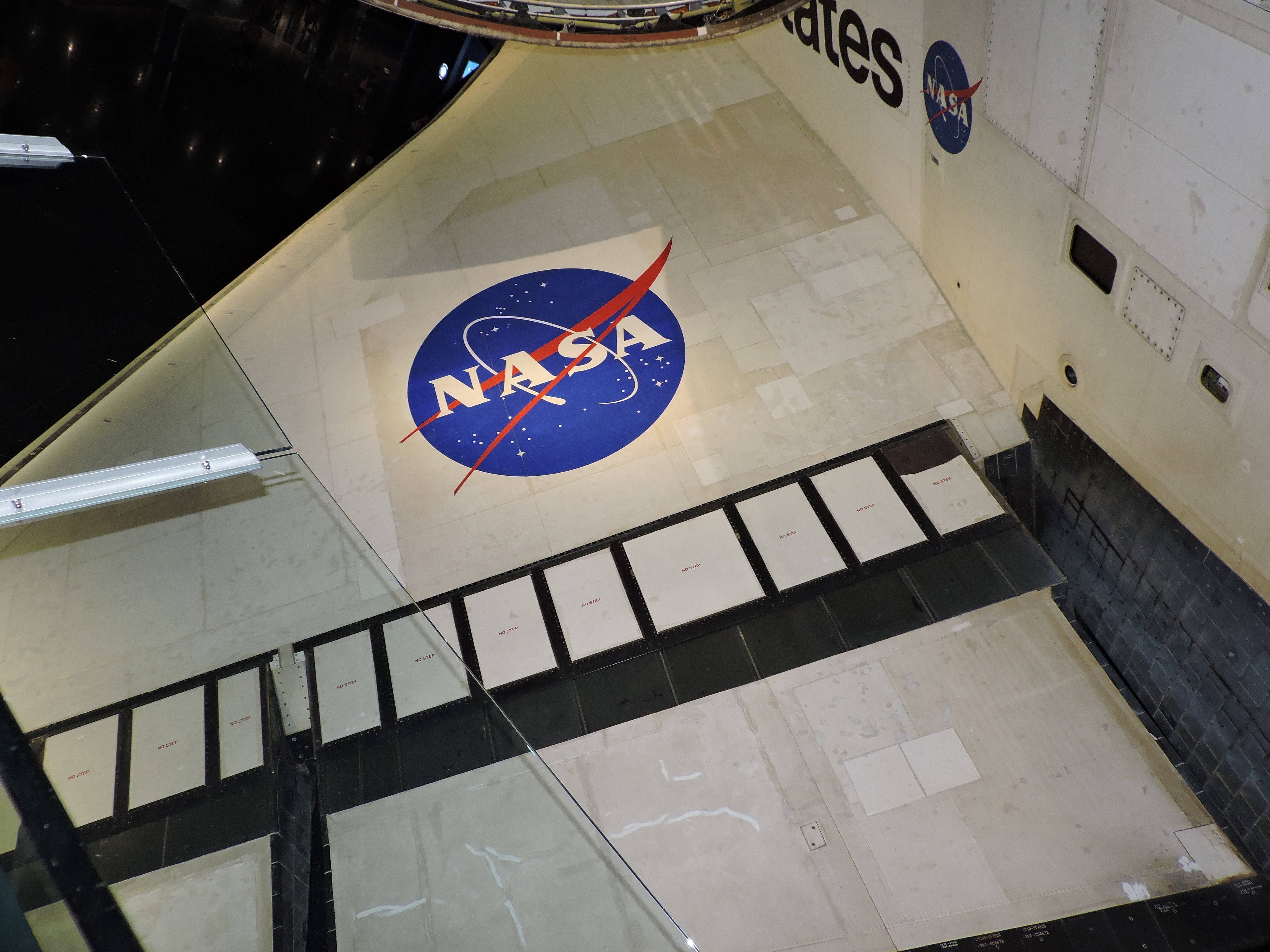 NASA 動態圖片 桌布 壁紙 — 從高角度觀看NASA標誌投射在太空船展覽館內的瓷磚地板上，設有玻璃屏障和白色牆壁。
