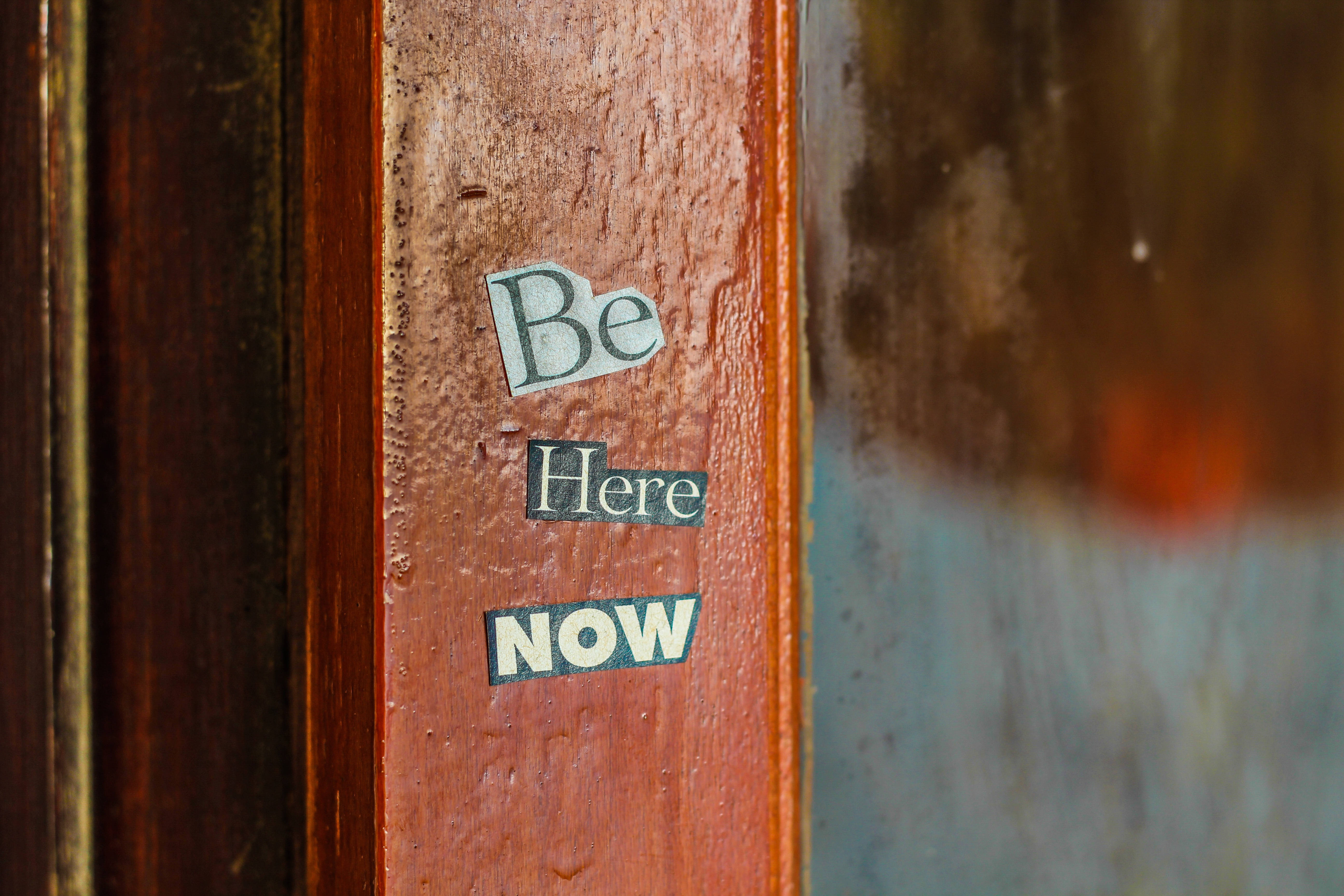 木紋 桌布 壁紙 — 復古 'Be Here Now' 貼紙的特寫，貼在風化的木門框上，色調溫暖，背景柔和。