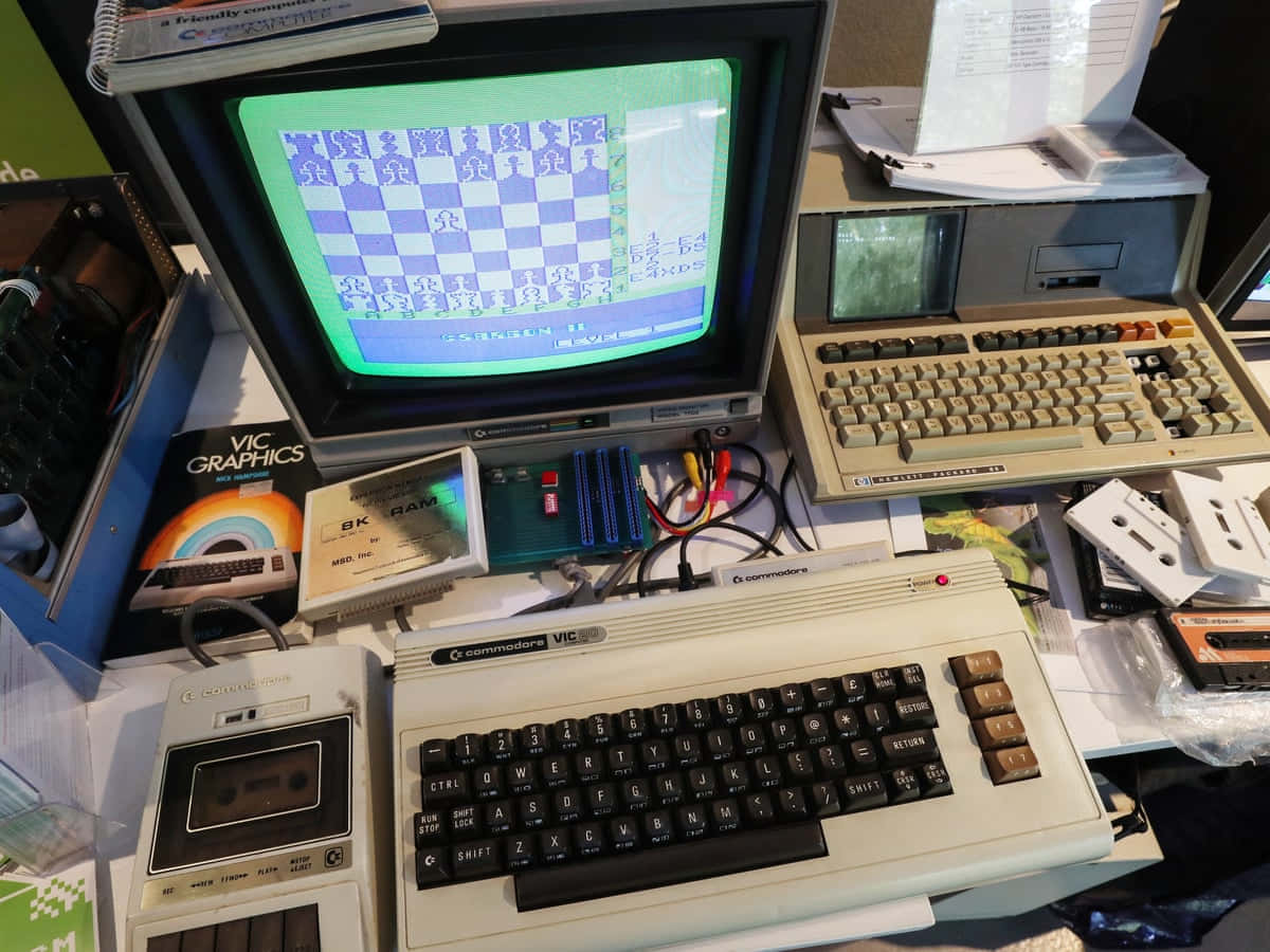 Old Pc 桌布 壁紙 — 復古 Commodore VIC-20 電腦在綠色螢幕上顯示西洋棋遊戲，周圍環繞著復古周邊設備和手冊。