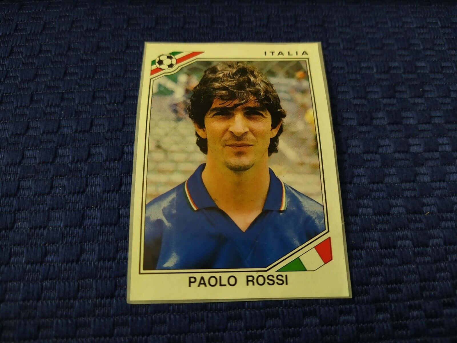 復古 桌布 壁紙 — 復古 Paolo Rossi 足球交換卡放置在帶有義大利國旗裝飾的紋理藍色布料上。