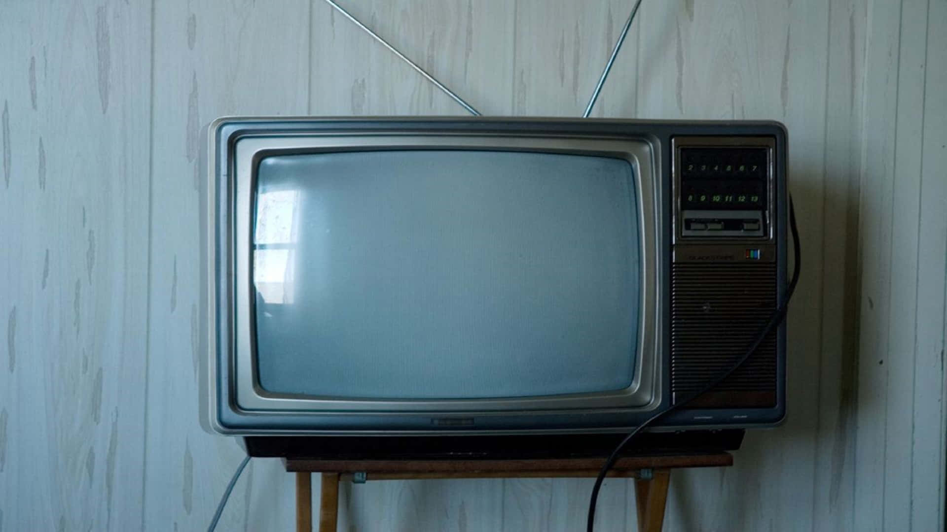 Television Set 桌布 壁紙 — 復古CRT電視機帶兔耳天線，置於木架上，背景為風化白牆。