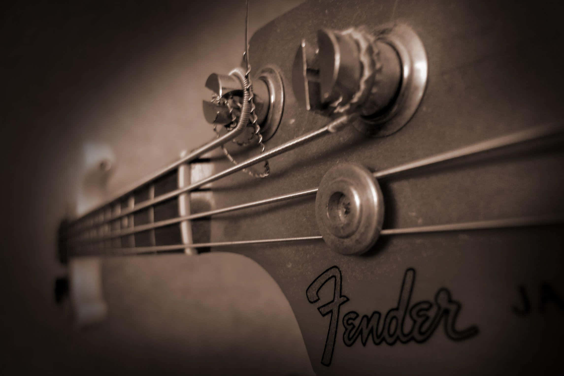 Bass Guitar 桌布 壁紙 — 復古Fender低音吉他琴頭特寫，帶有琴弦和調音旋鈕，呈現溫暖的懷舊棕色調。
