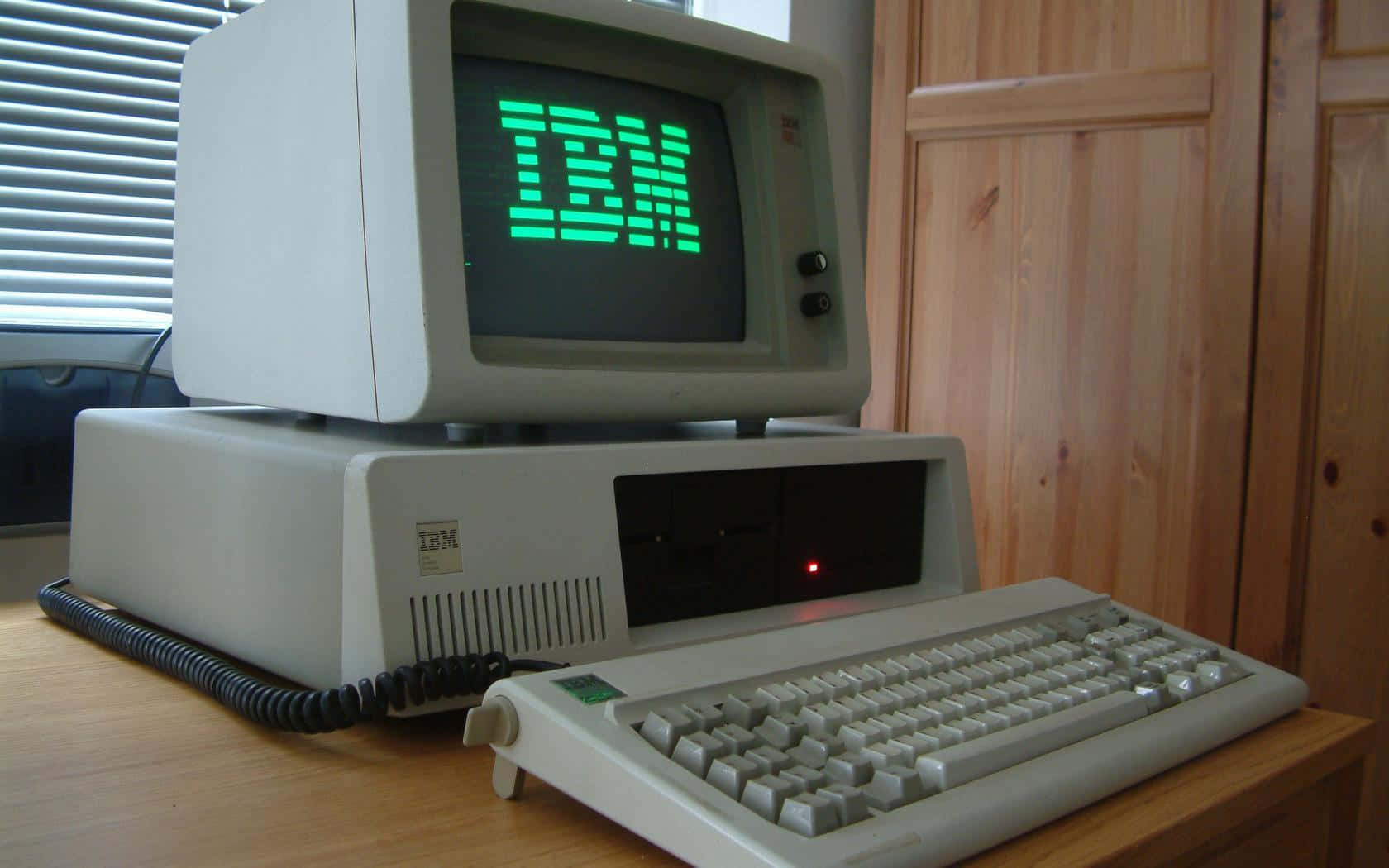 Old Pc 桌布 壁紙 — 復古IBM個人電腦，螢幕上帶有綠色發光標誌，放置在木桌上，旁邊有鍵盤和木櫃。