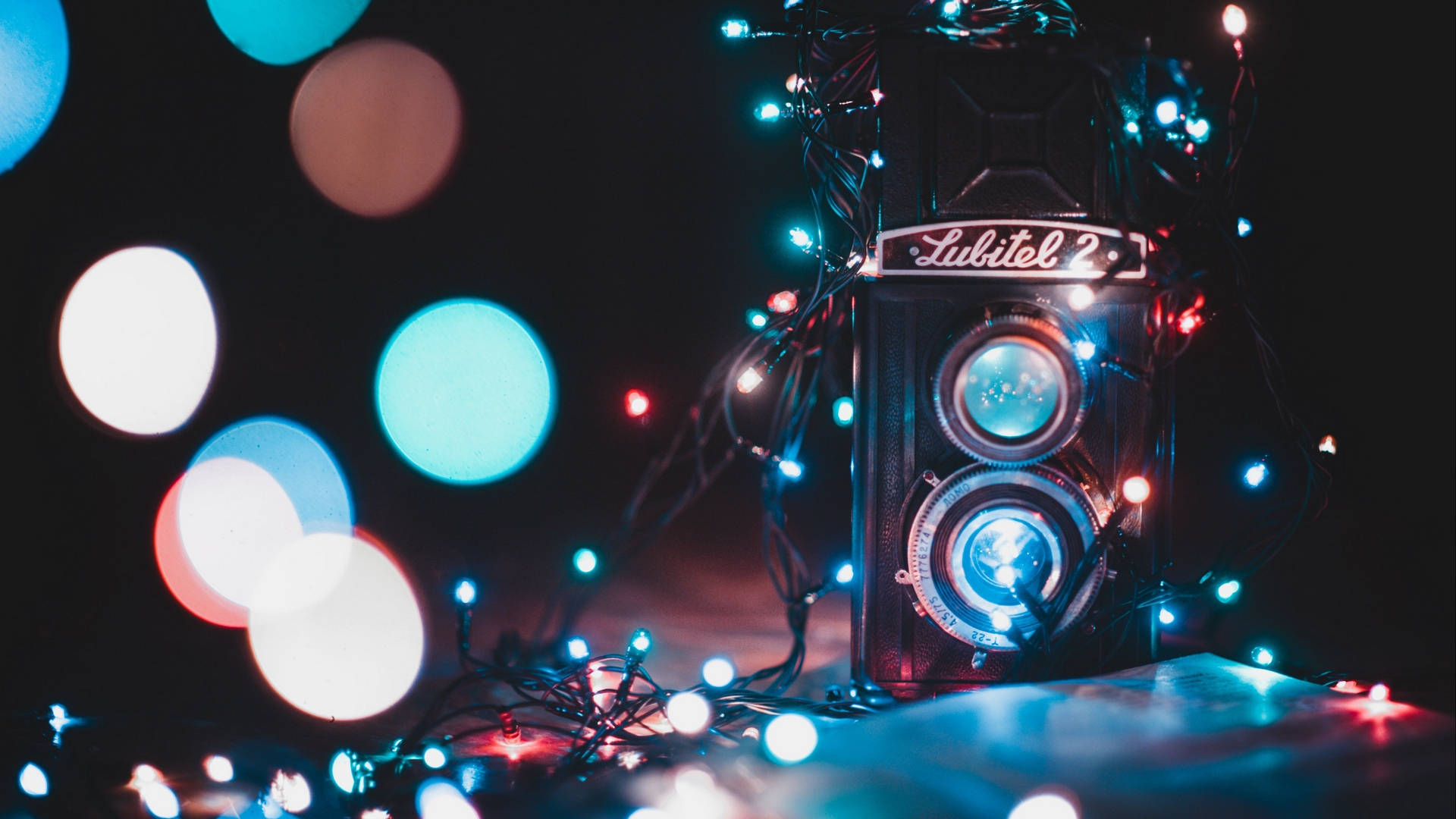 復古美學 桌布 壁紙 — 復古Lubitel 2相機包裹在閃爍的仙女燈中，背景黑暗，帶有彩色散景圓圈。