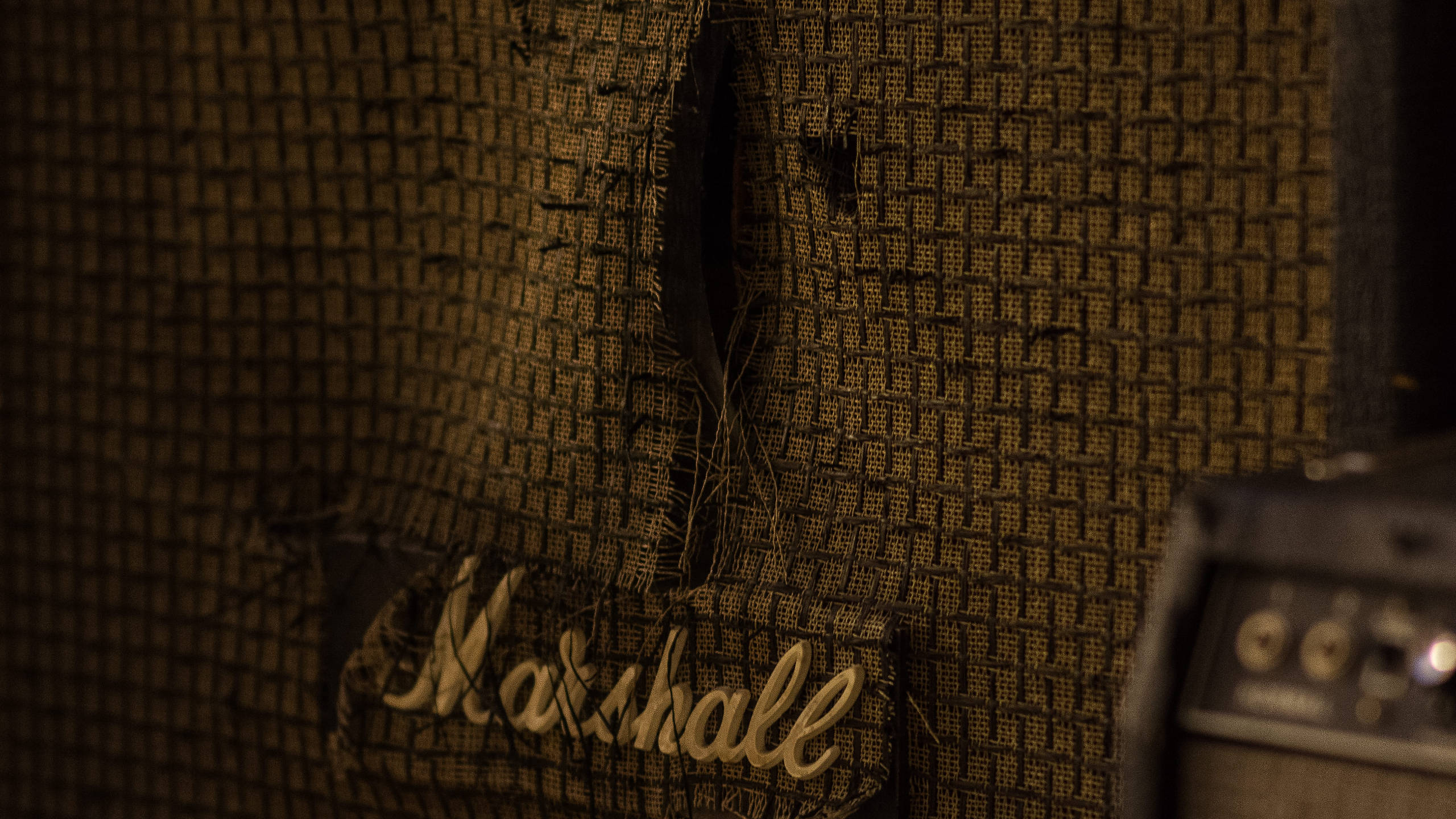 Marshall 桌布 壁紙 — 復古Marshall吉他音箱特寫，磨損的網格布和溫暖燈光下發光的標誌。
