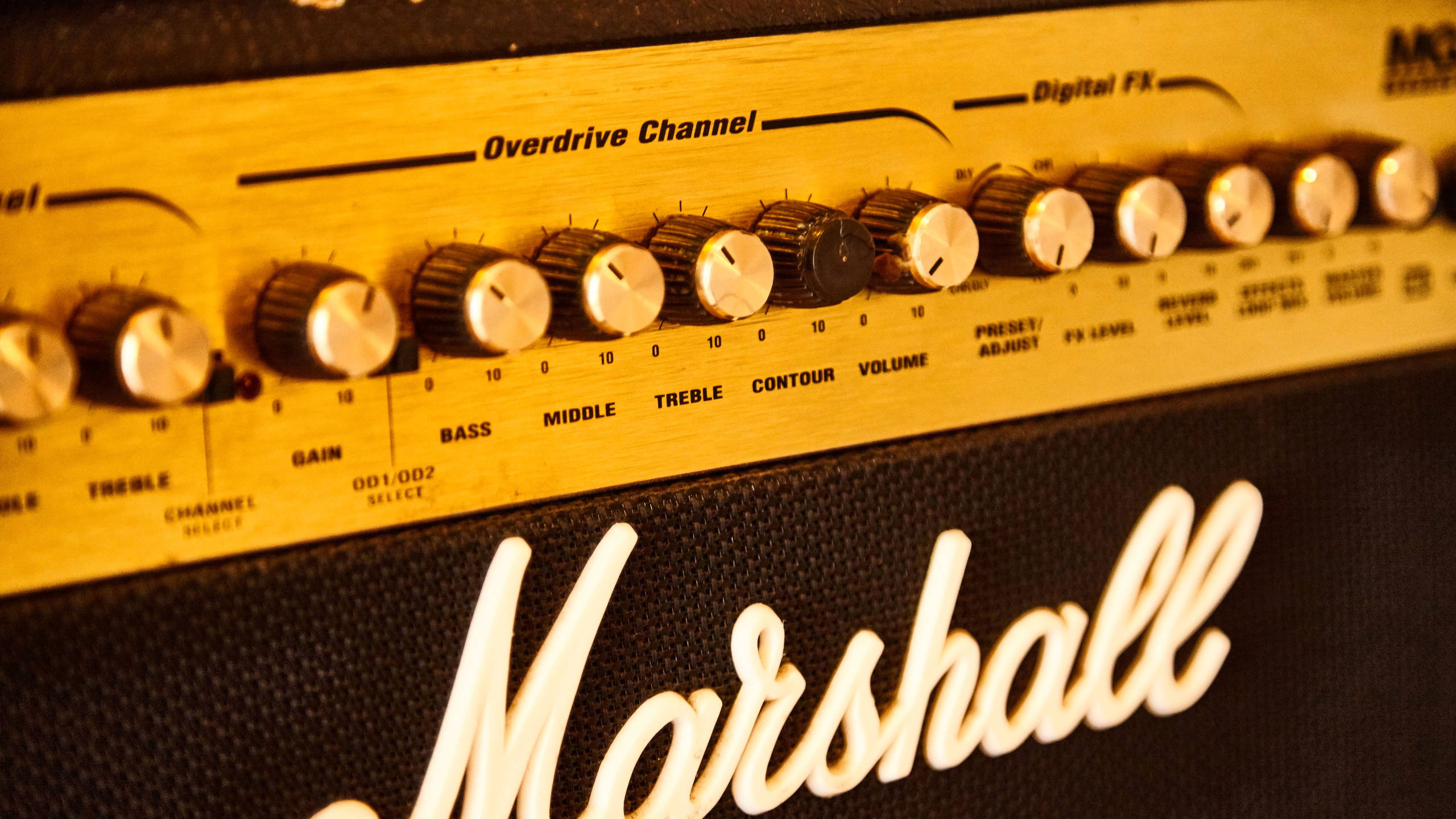 Marshall 桌布 壁紙 — 復古Marshall吉他音箱特寫，金色旋鈕和發光白色標誌，在溫暖燈光下。