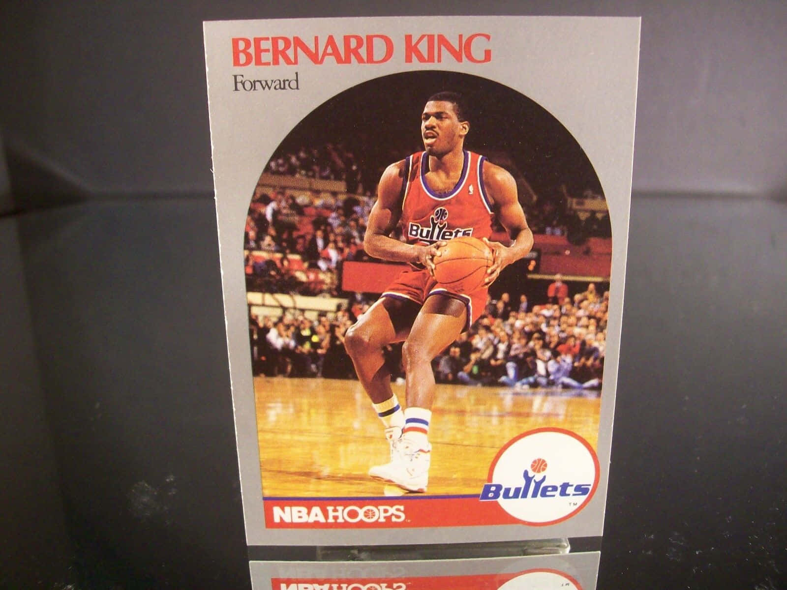 Athletic 桌布 壁紙 — 復古NBA Hoops球星卡，展示Bernard King身穿紅色子彈隊球衣在硬木球場上運球，背景有觀眾。