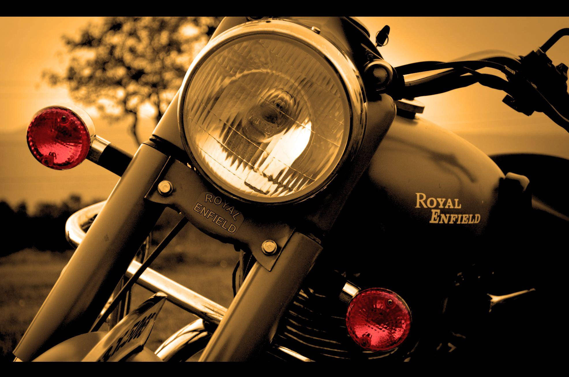 Royal 桌布 壁紙 — 復古Royal Enfield機車頭燈在金色日落背景下溫暖發光的特寫。