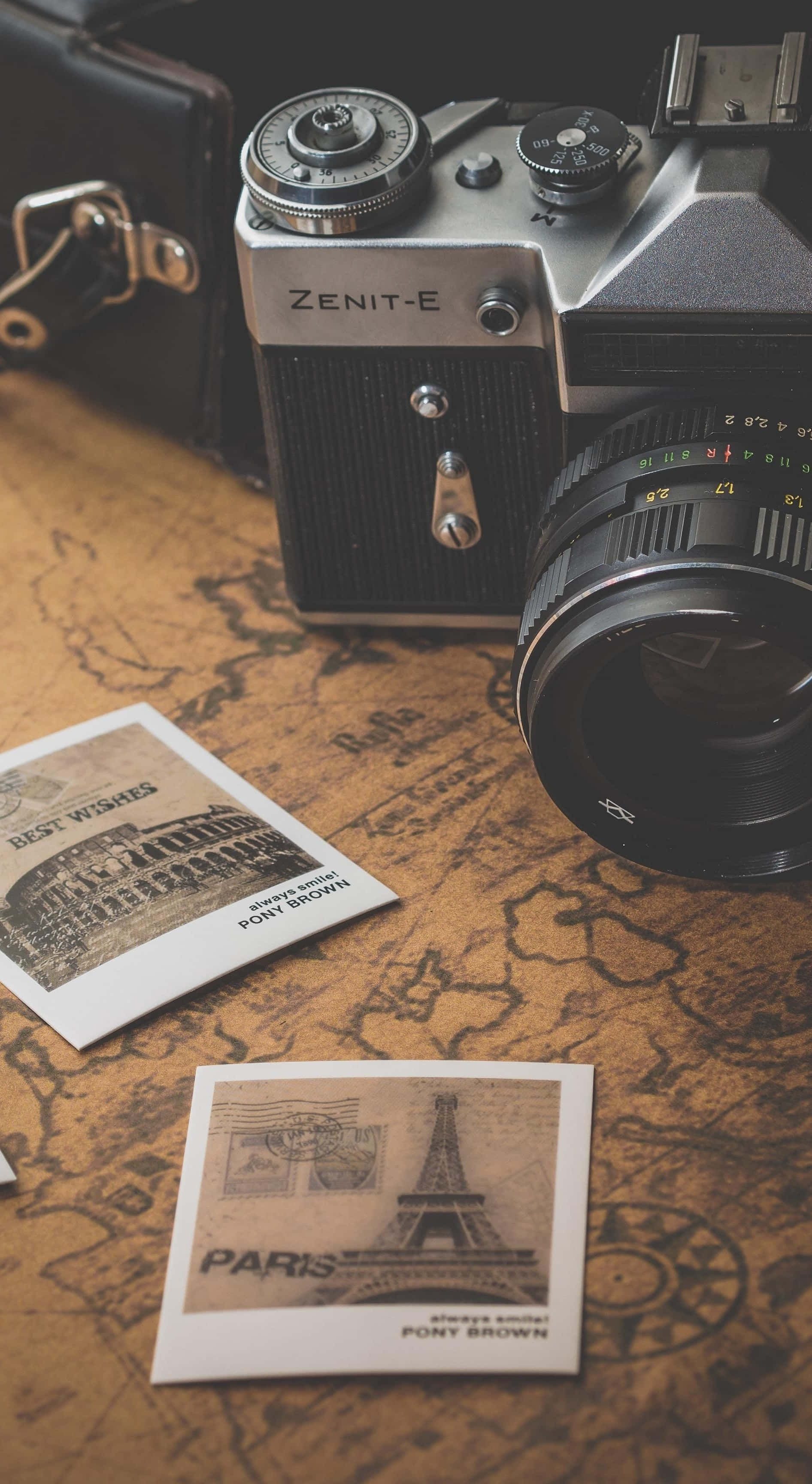 Travel Aesthetic Phone 桌布 壁紙 — 復古Zenit-E底片相機放在一張舊地圖上，旁邊是帶有懷舊色調和皮革裝飾的巴黎主題明信片。