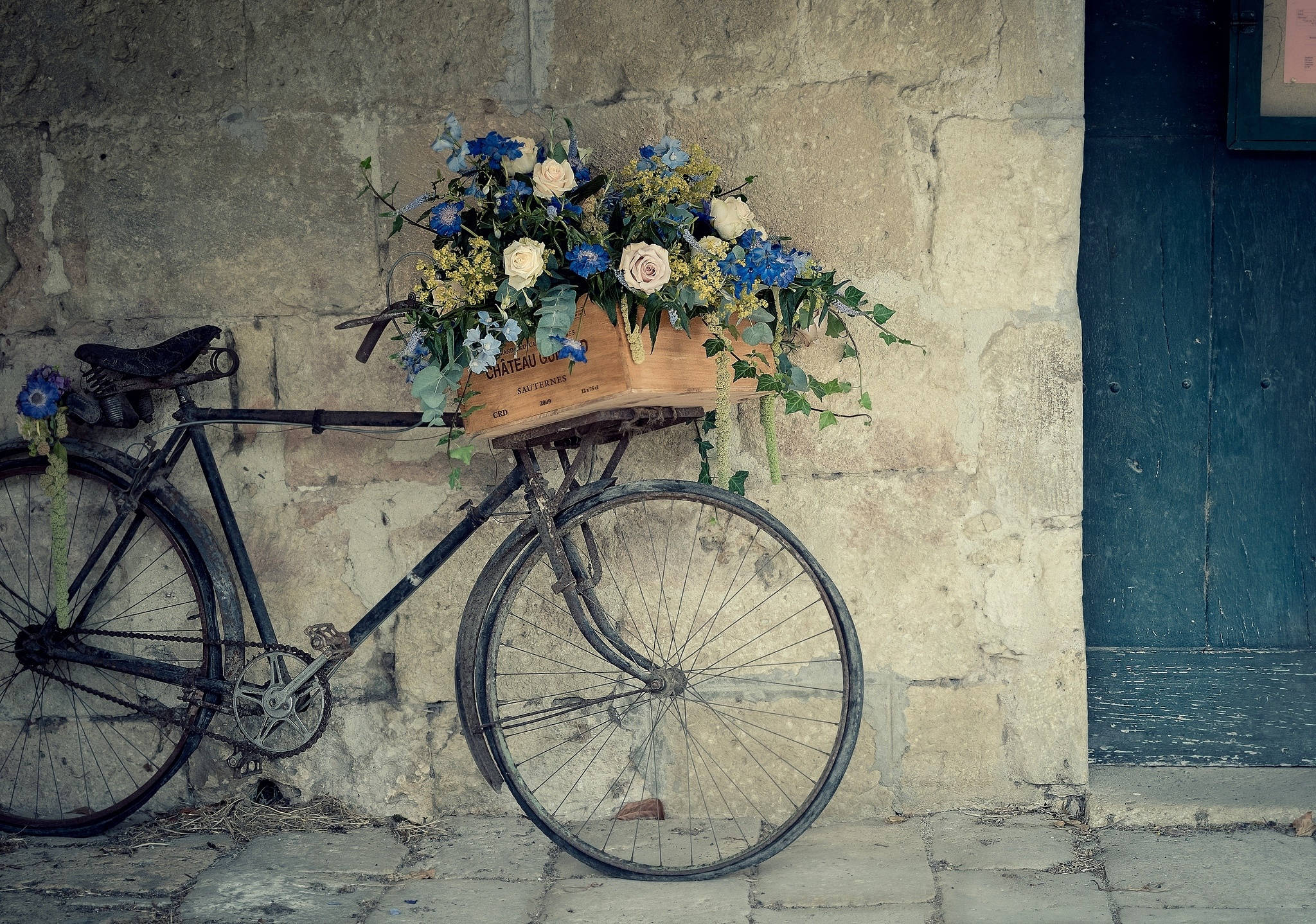 Bicycle 桌布 壁紙 — 復古單車載著花籃，靠在青綠色門邊的風化石牆上。