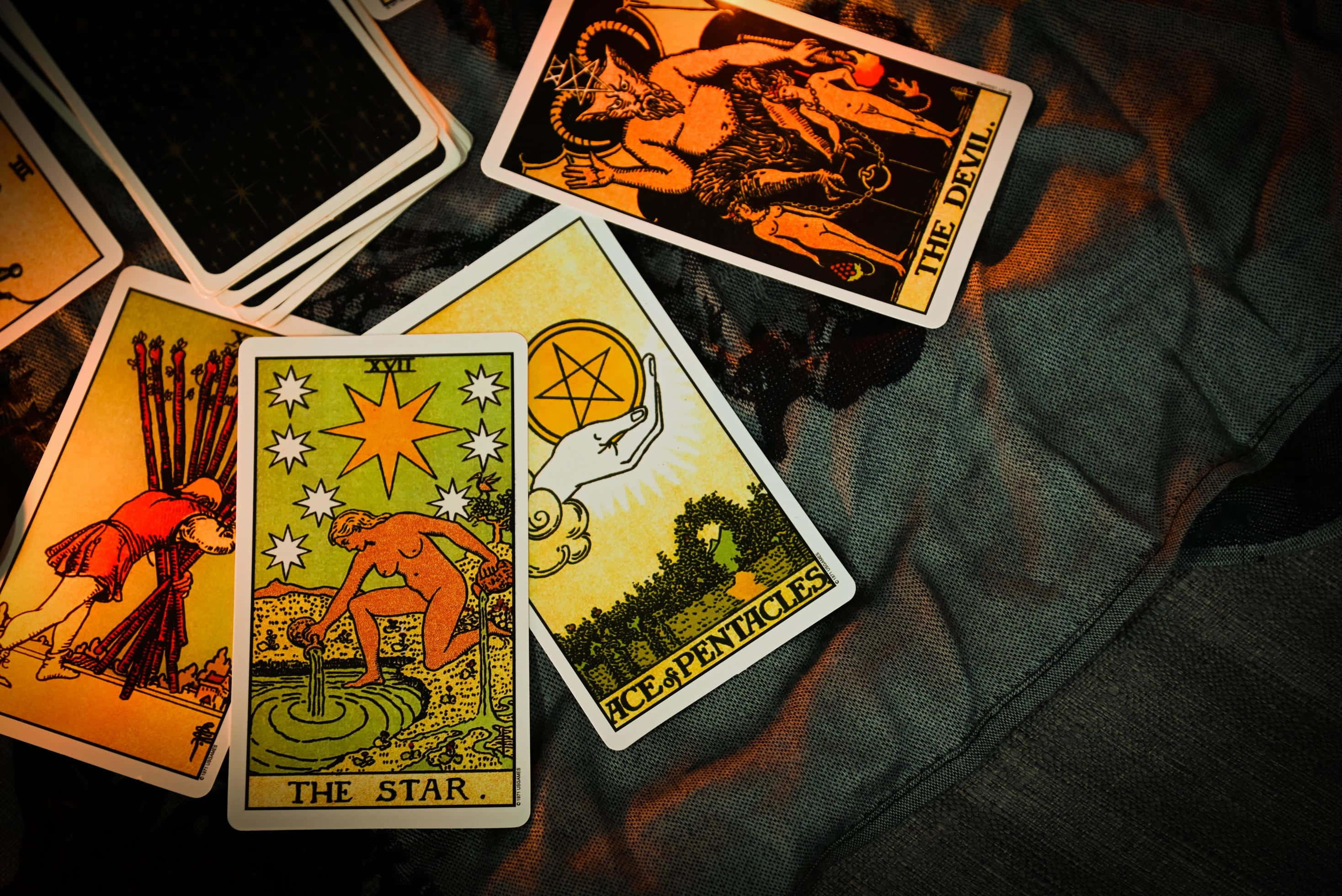 Tarot Card 桌布 壁紙 — 復古塔羅牌，包括星星、惡魔和錢幣王牌，在溫暖燈光下放置於深色紋理布料上。