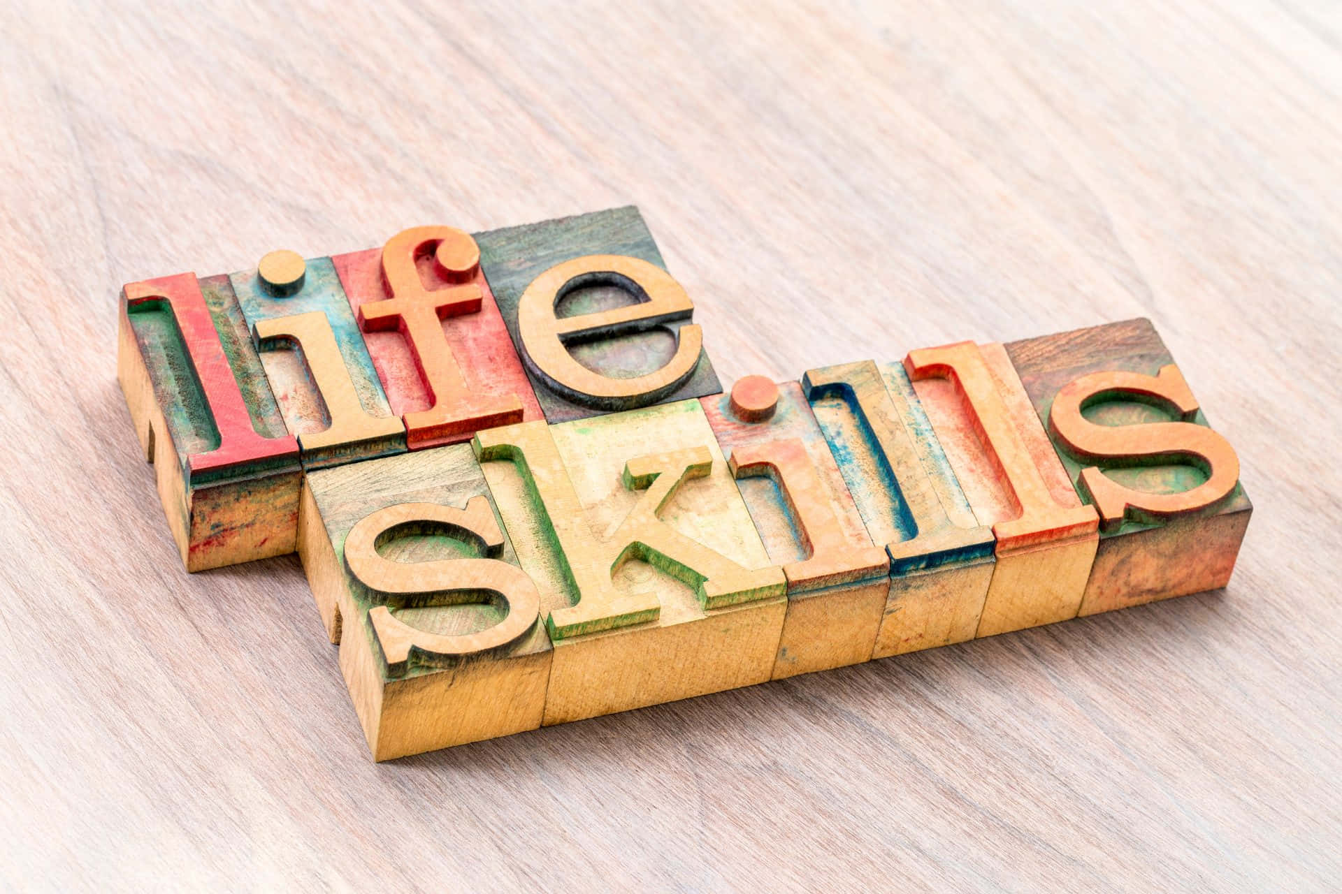 life 桌布 壁紙 — 復古彩色活字塊拼出「life skills」，放在溫暖的木質表面上。