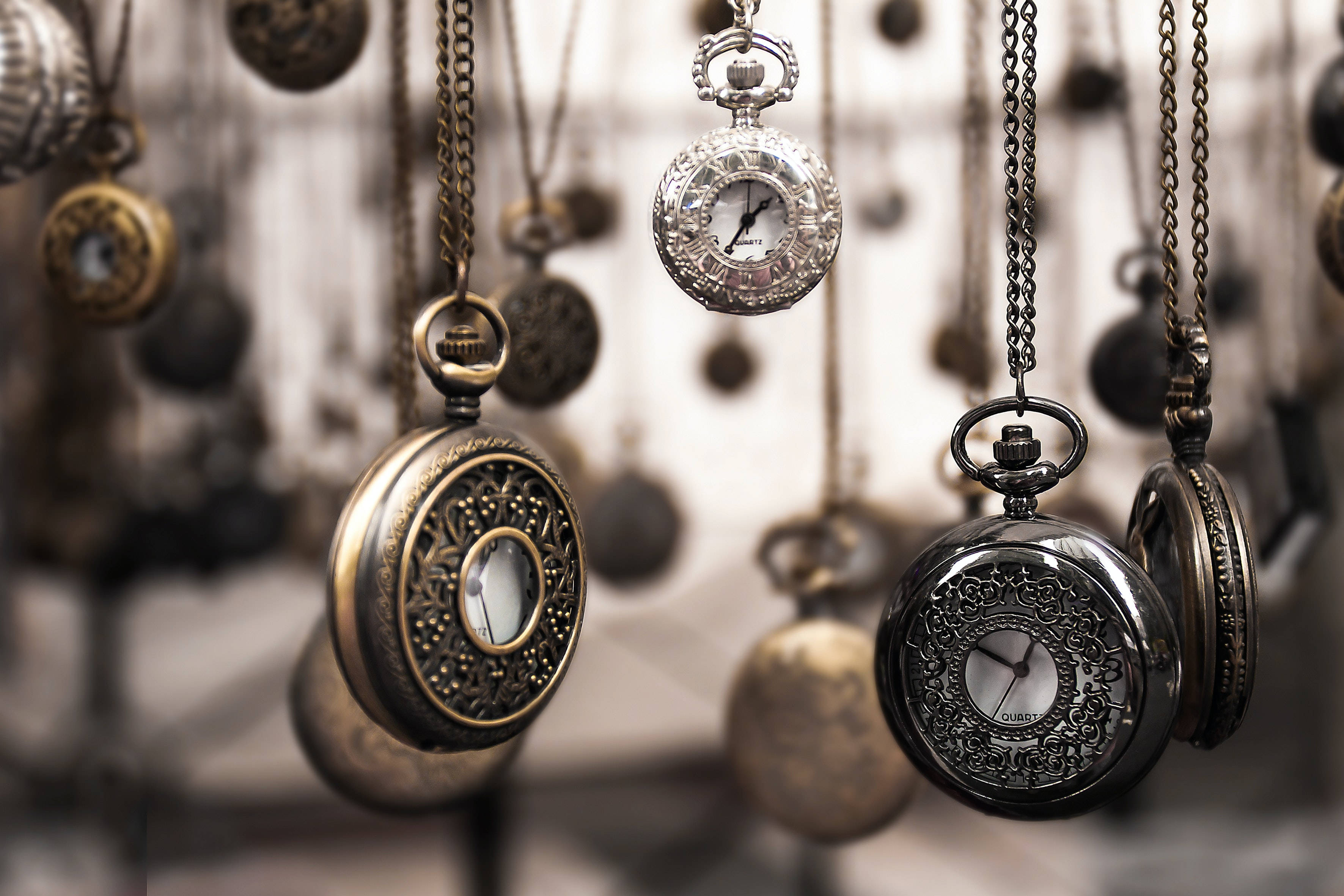Gold Jewellery 桌布 壁紙 — 復古懷錶懸掛在柔焦中，其華麗的黃銅和銀色錶殼捕捉柔和光線。