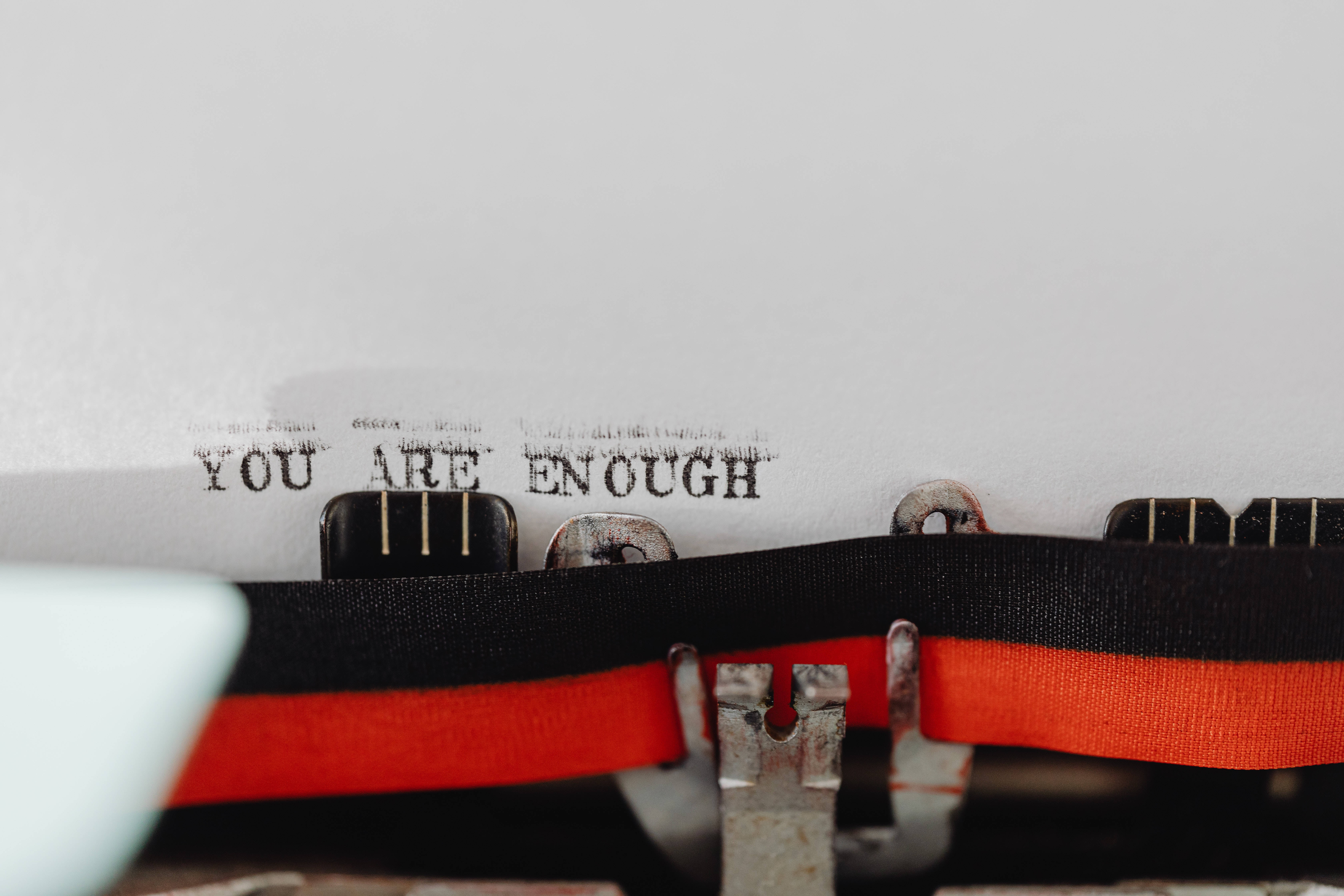 Inspirational Quotes 桌布 壁紙 — 復古打字機的特寫，白色紙上打有「YOU ARE ENOUGH」字樣，並以紅色絲帶點綴。