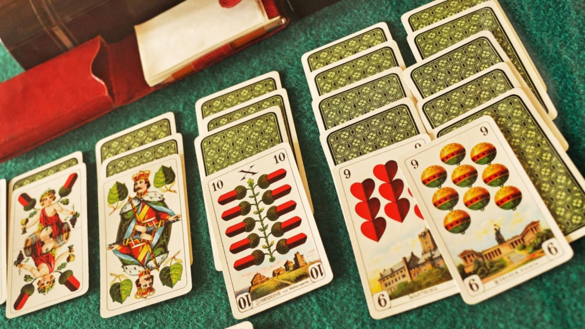 Solitaire 桌布 壁紙 — 復古撲克牌，帶有華麗插圖和綠色圖案背面，在綠色氈面上呈扇形展開。