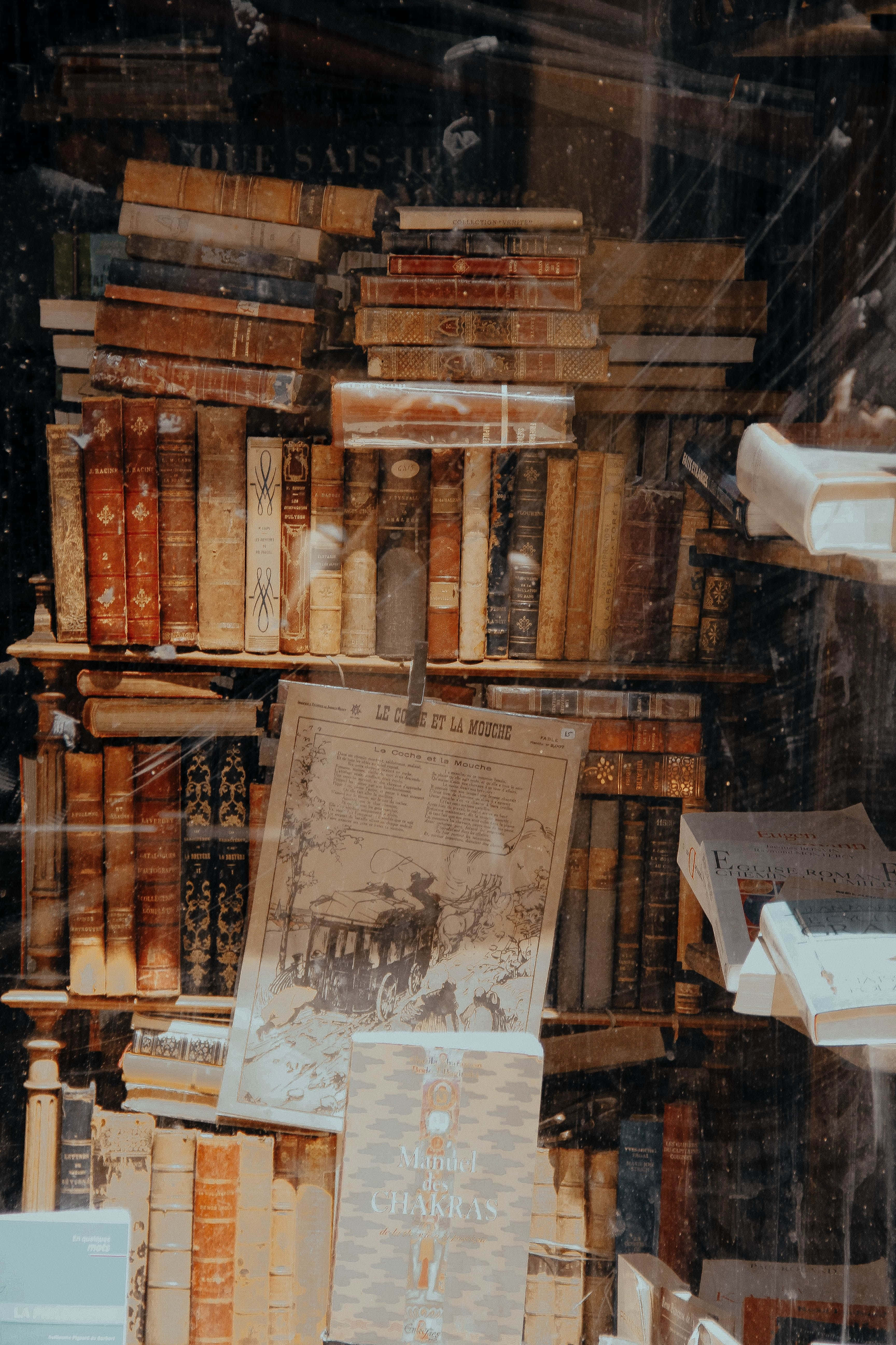 Dark Academia Aesthetic 桌布 壁紙 — 復古書籍雜亂地堆疊在佈滿灰塵的商店櫥窗中，帶有褪色的報紙和玻璃反射。