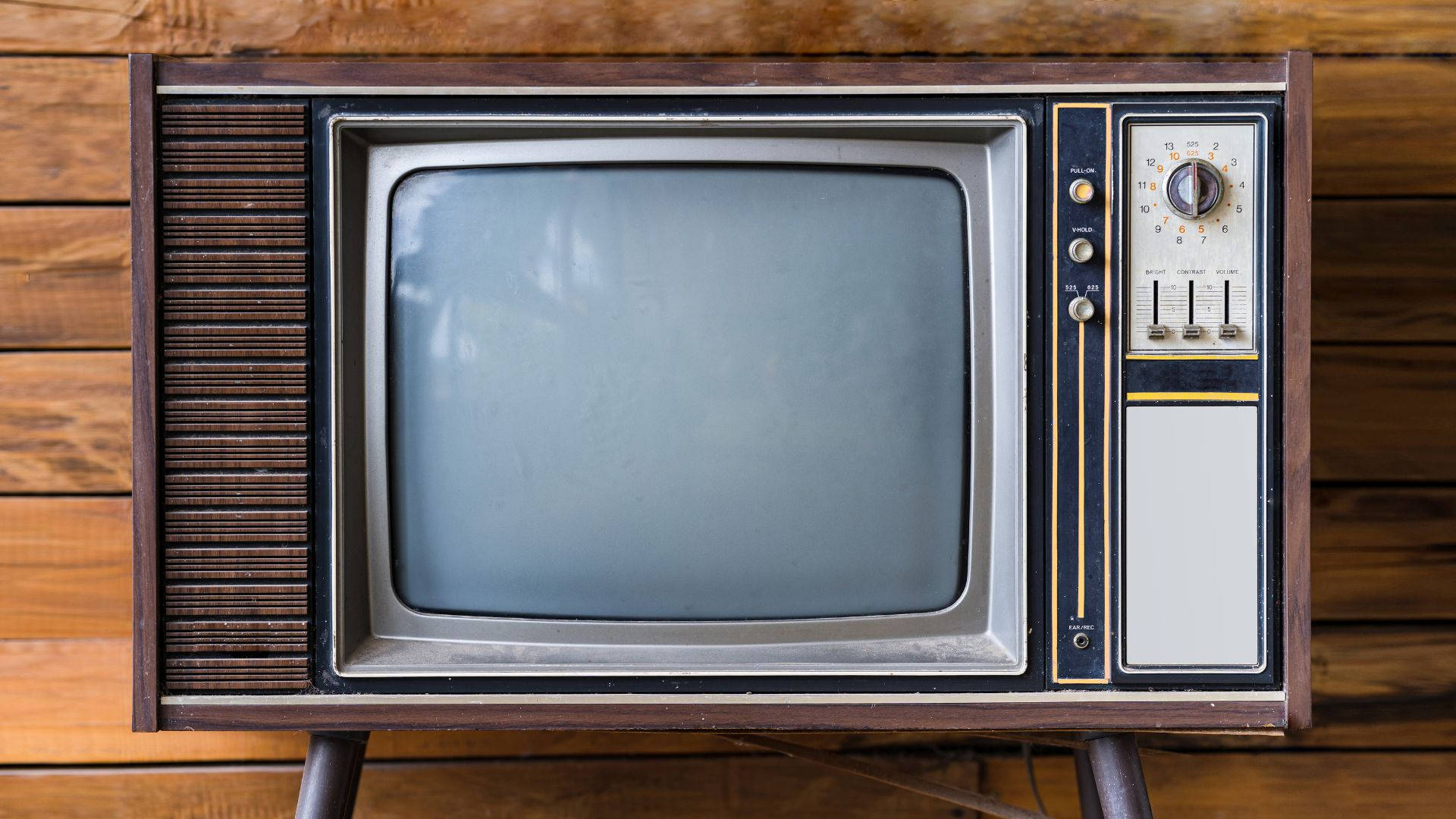 tv 桌布 壁紙 — 復古木製電視機，帶有銀色框架和旋鈕，放置在溫暖的木鑲板牆上。