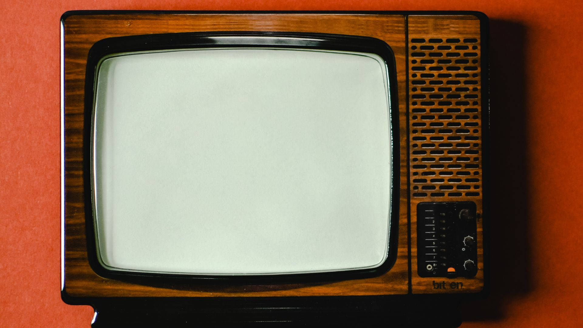 tv 桌布 壁紙 — 復古木製電視機，空白螢幕靠在溫暖的橙色牆上，投下柔和陰影。