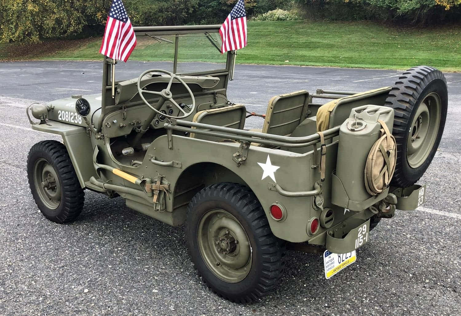 Jeep Willys 桌布 壁紙 — 復古橄欖綠軍用吉普車，掛有美國國旗，停在草地附近的瀝青路上。