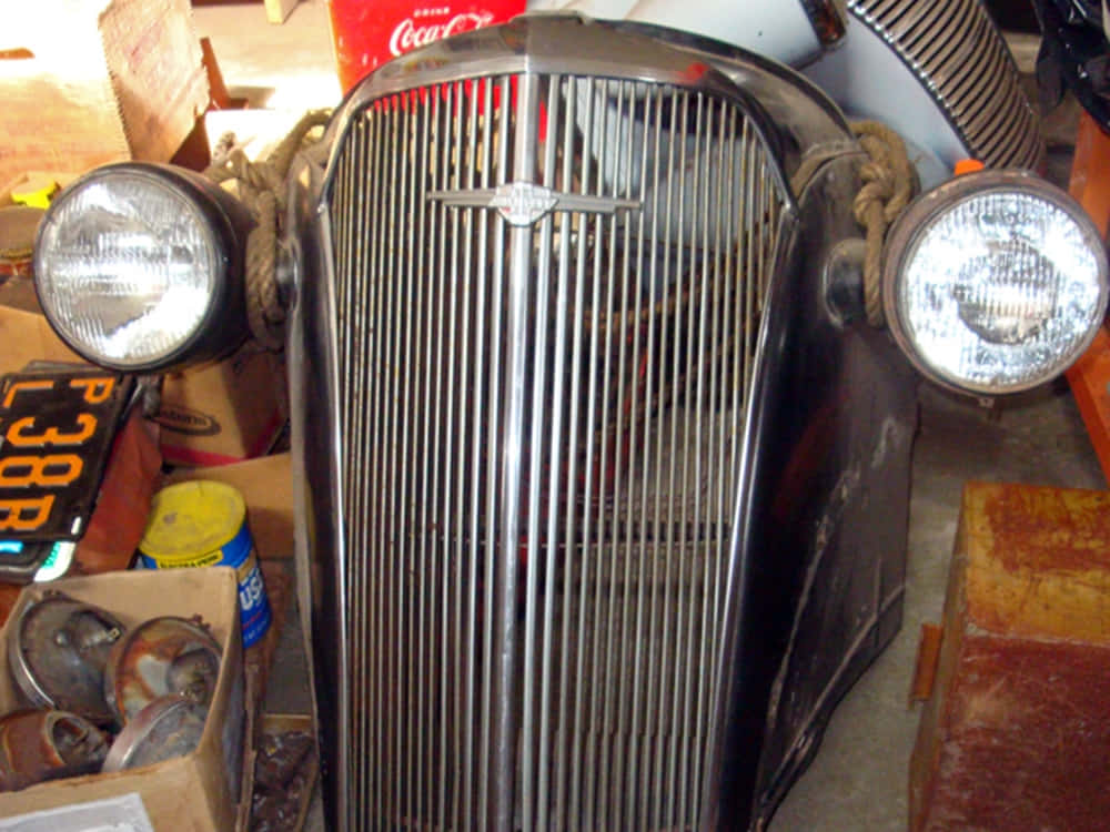 Car Grill 桌布 壁紙 — 復古汽車格柵，帶有鍍鉻垂直條和圓形頭燈，周圍是雜亂的車庫物品。