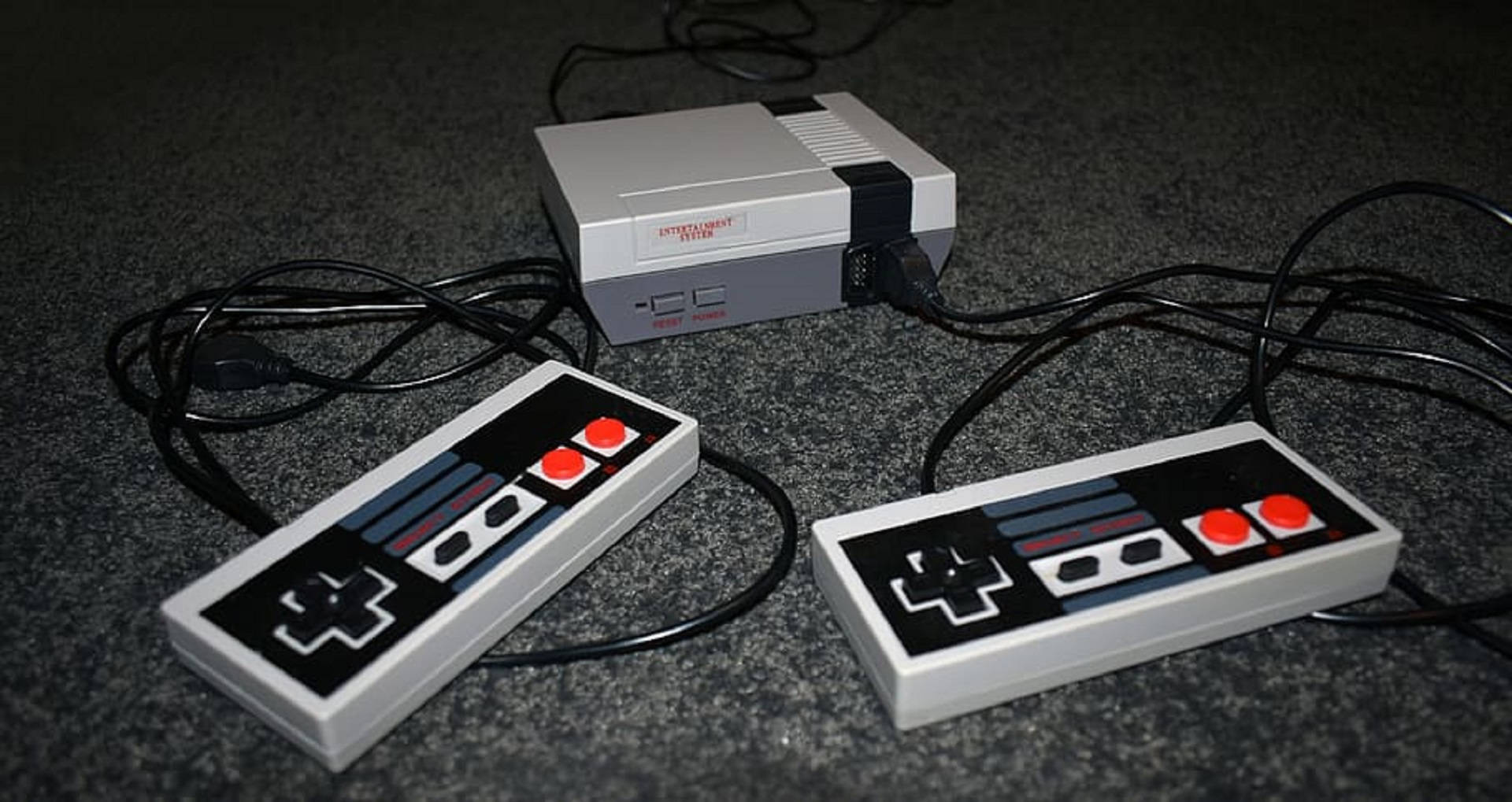紅白機 桌布 壁紙 — 復古灰色 Nintendo Entertainment System 主機連同兩個控制器放在深色地毯上。
