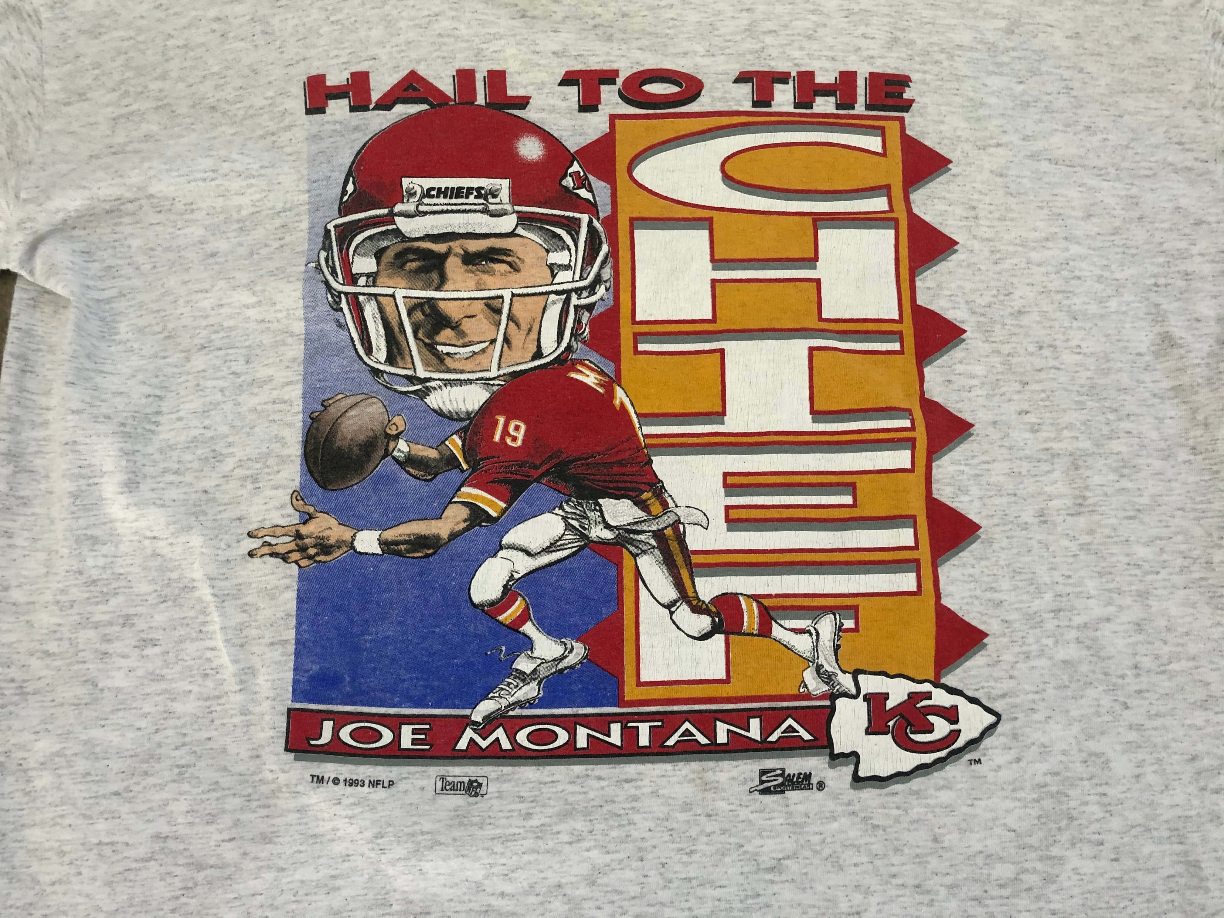 Joe Montana 桌布 壁紙 — 復古灰色T恤，印有卡通插圖，描繪喬·蒙塔納身穿紅色酋長隊球衣投擲橄欖球，並帶有「Hail to the Chief」字樣。