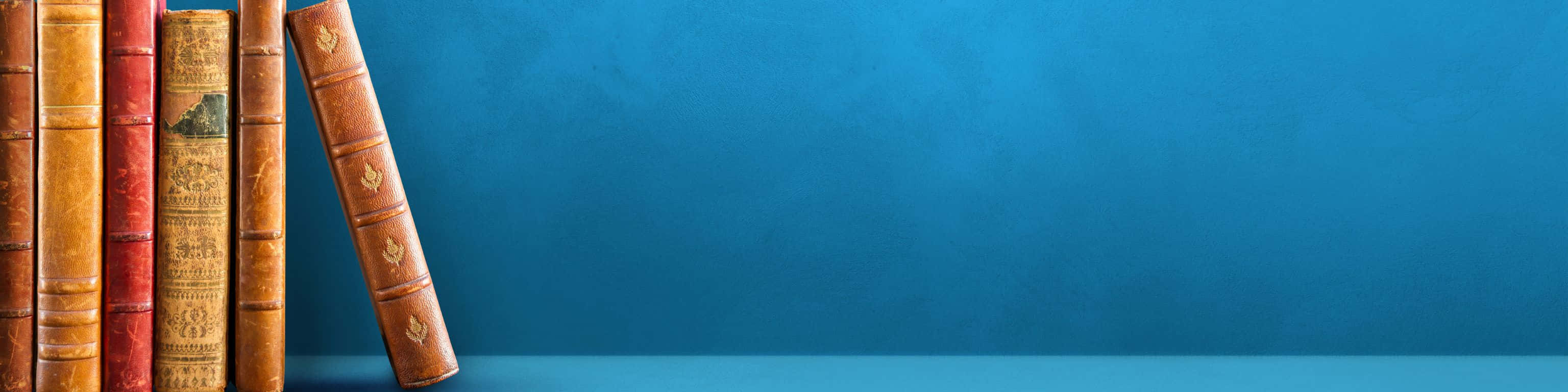 3072x768 桌布 壁紙 — 復古皮革裝訂書籍在純色青綠色背景上直立，光線柔和。