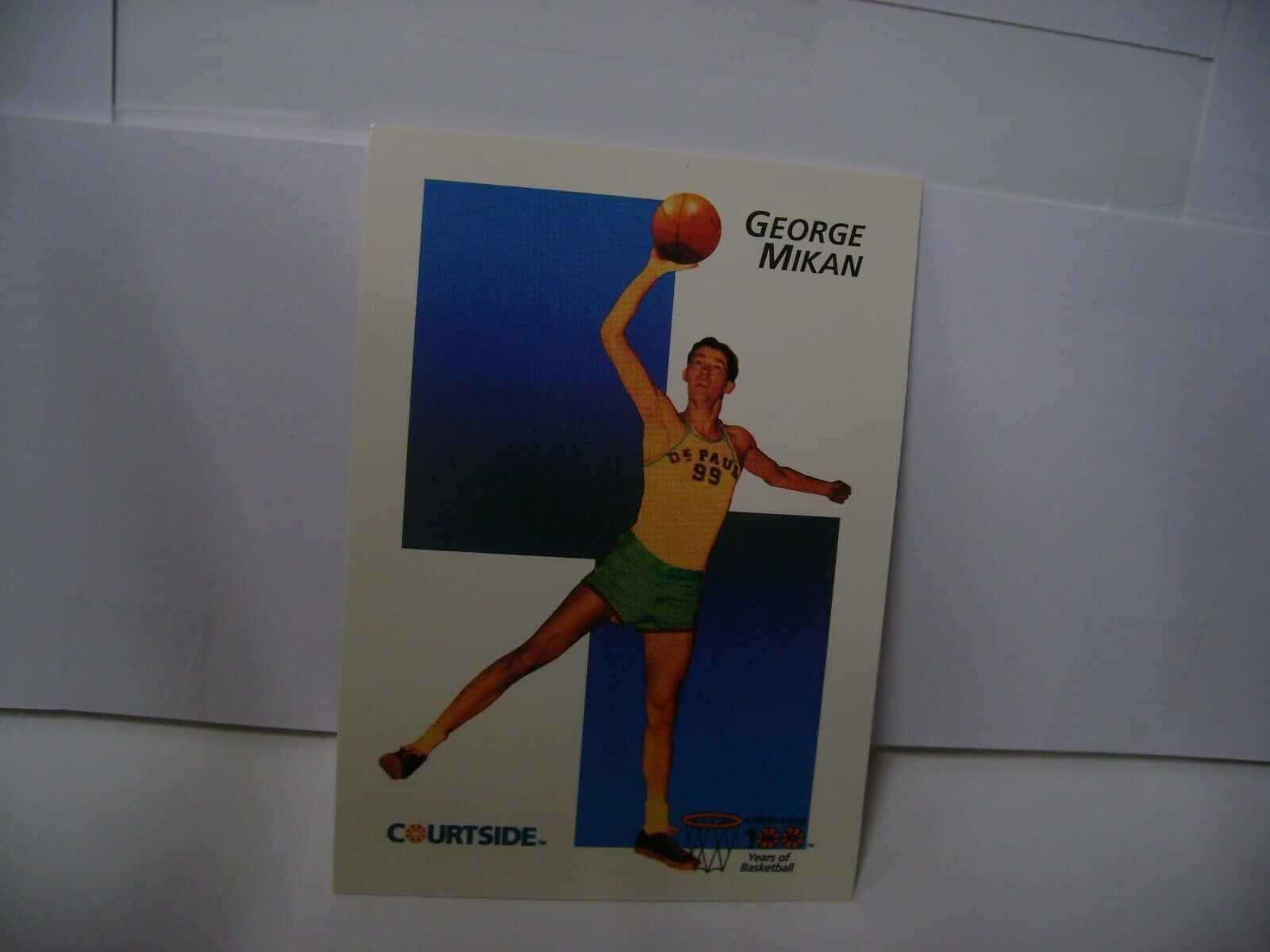 籃球 桌布 壁紙 — 復古籃球卡 featuring George Mikan 身穿黃色球衣和綠色短褲，在藍色背景下持球。