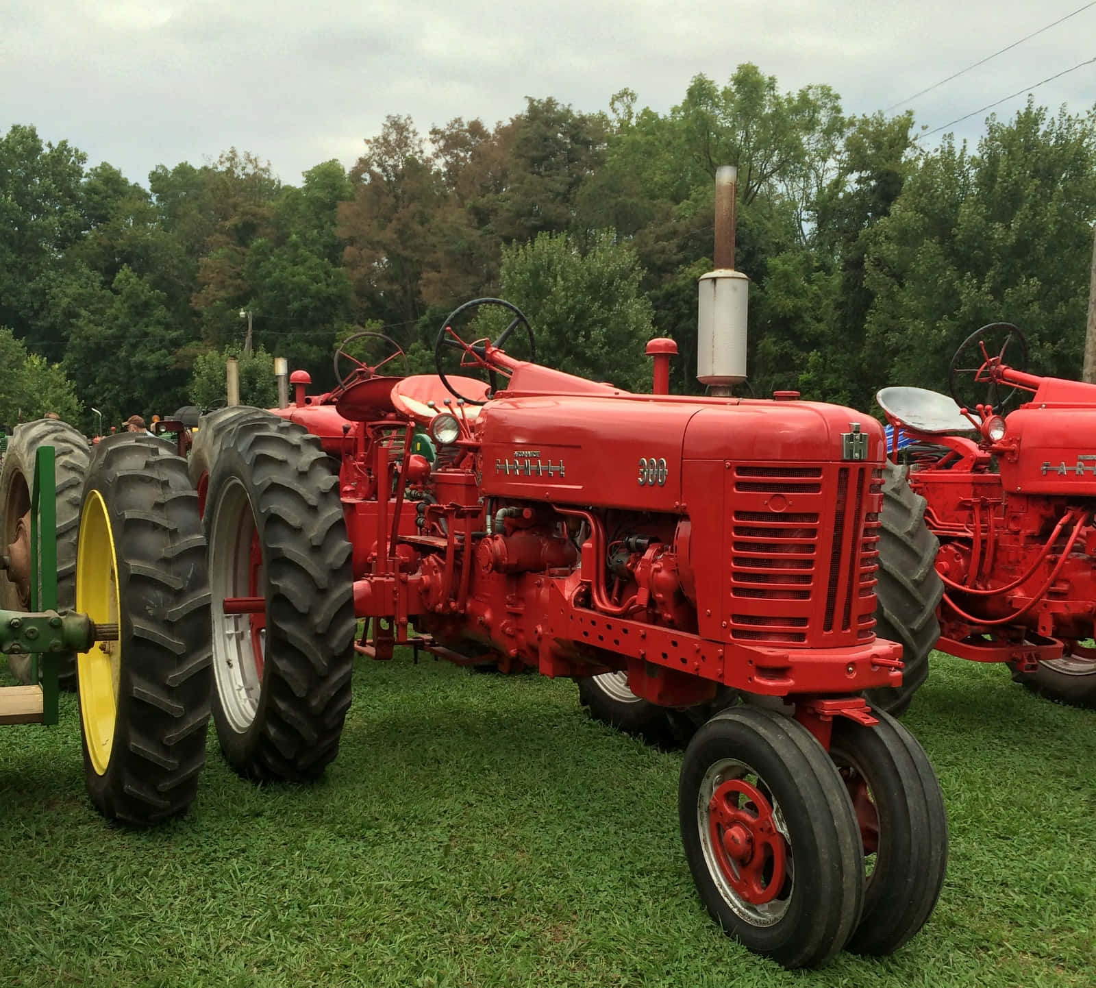 Tractor 桌布 壁紙 — 復古紅色 Farmall 拖拉機配黃色輪胎，停泊在陰天下的綠色草地上。