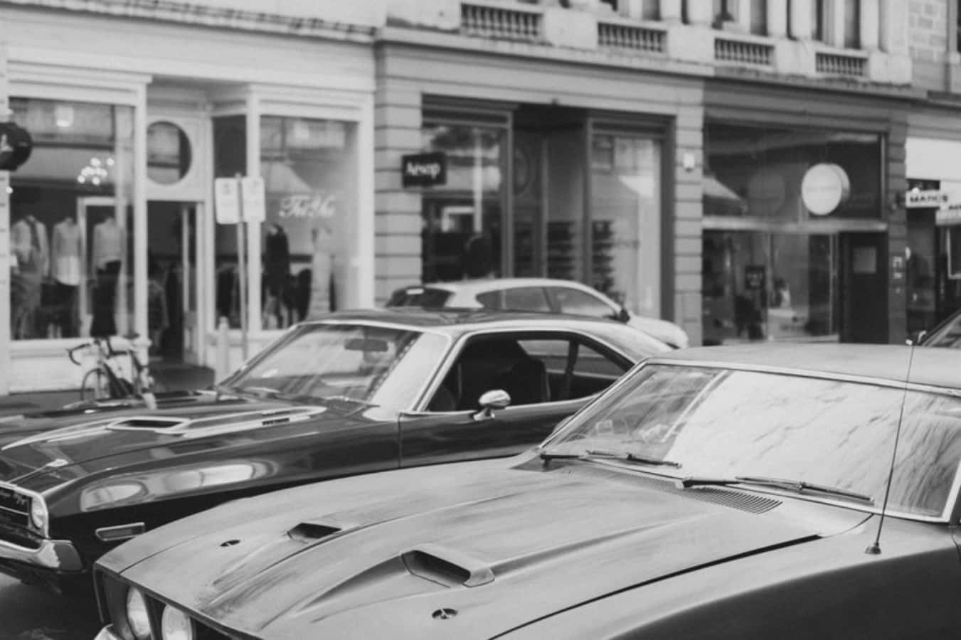 Muscle Cars 桌布 壁紙 — 復古肌肉車停泊在黑白城市街道上，旁邊有商店門面和腳踏車。