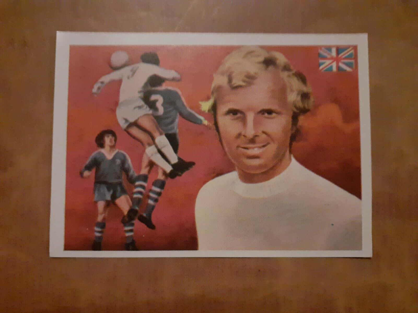 poster 桌布 壁紙 — 復古足球交換卡，上面有一個微笑的金髮男子穿著白色毛衣，兩名球員在紅色背景和英國國旗上行動。