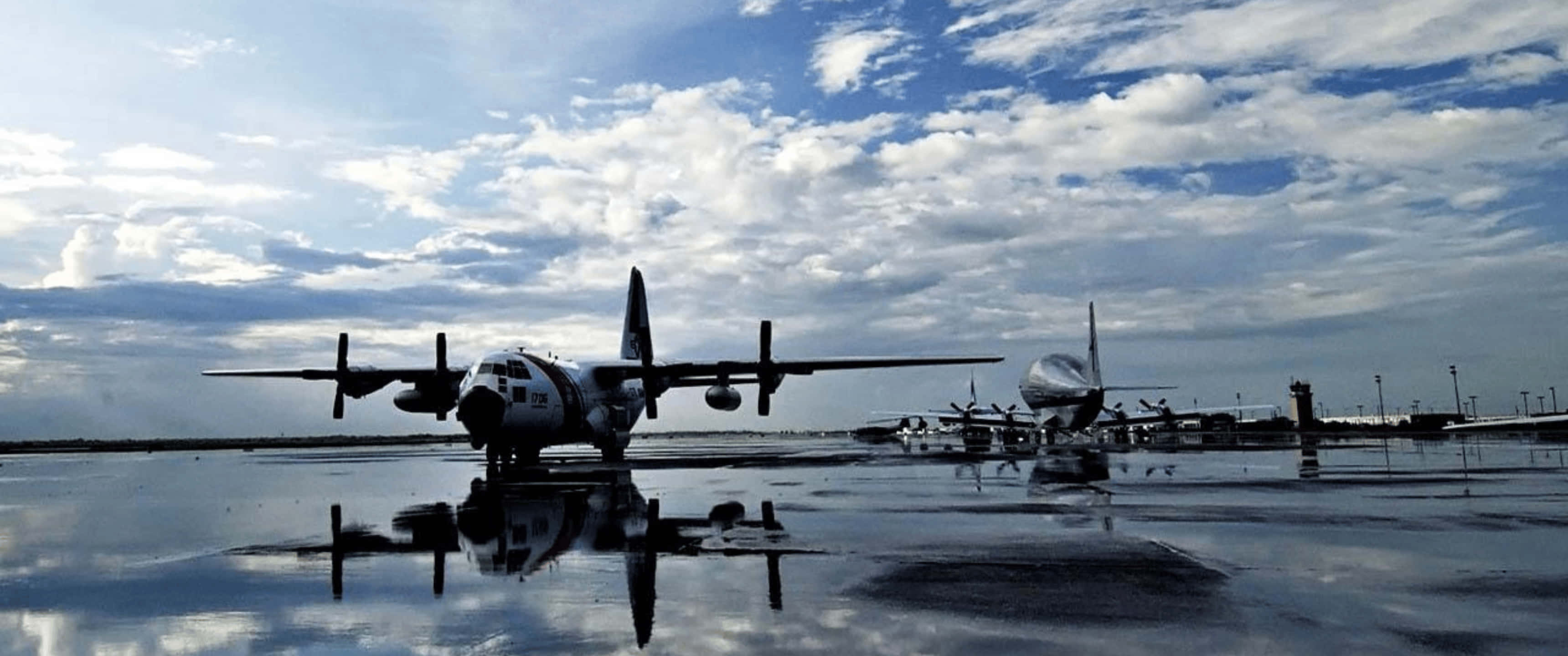 Plane 桌布 壁紙 — 復古軍用飛機在陰雲密布的天空下形成剪影，倒映在機場濕漉漉的停機坪上。