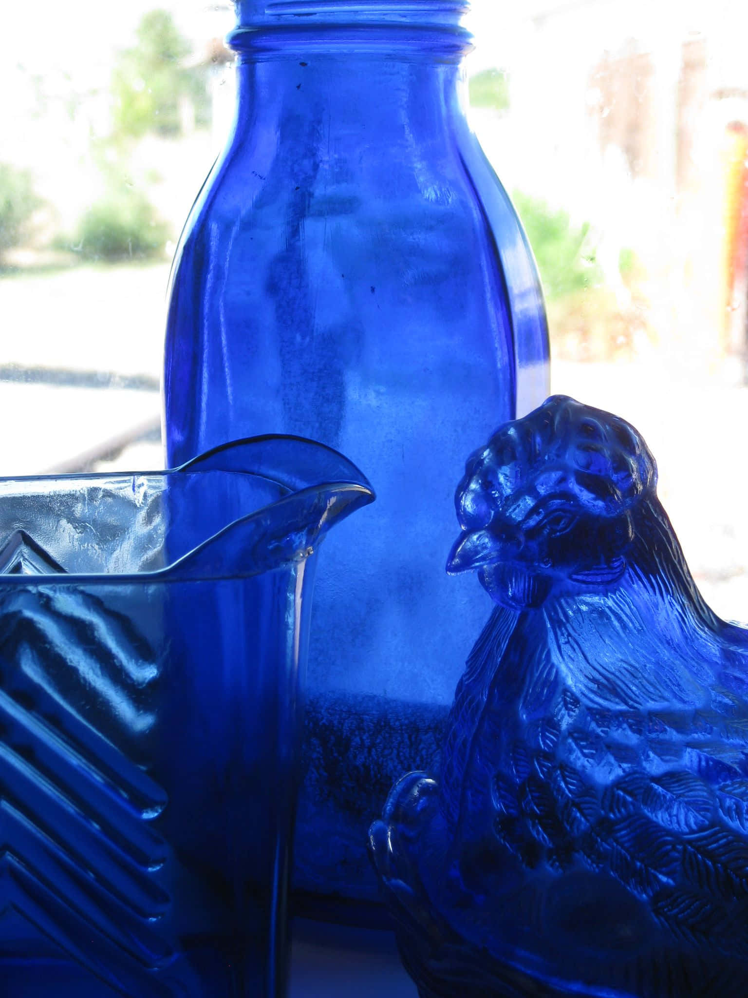Cobalt Blue 桌布 壁紙 — 復古鈷藍色玻璃器皿，包括一個瓶壺和一個小雞雕像，沐浴在柔和自然光中。