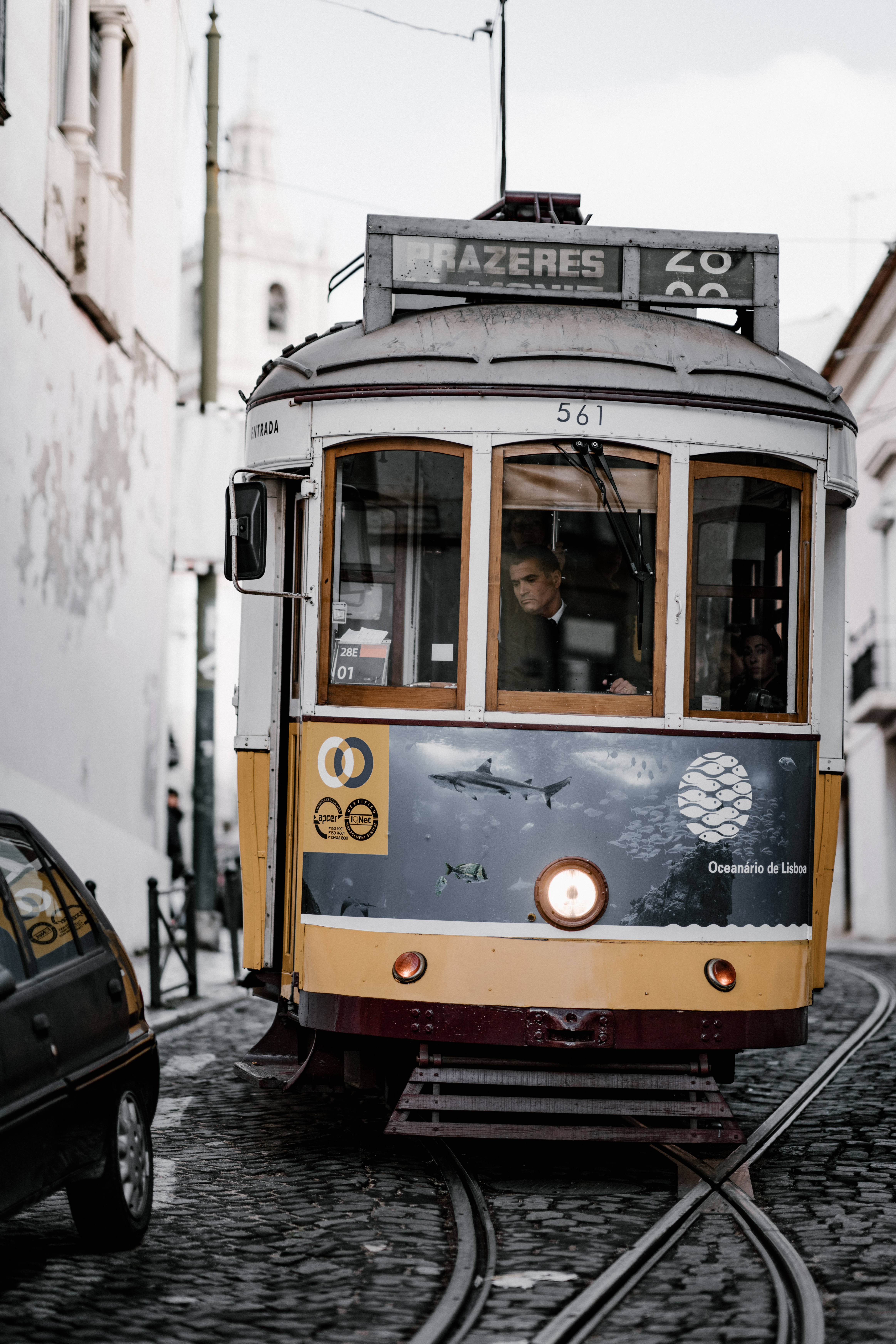 Portugal 桌布 壁紙 — 復古黃色電車帶有海洋主題廣告，在陰天下行駛於兩旁白色建築的鵝卵石街道上。