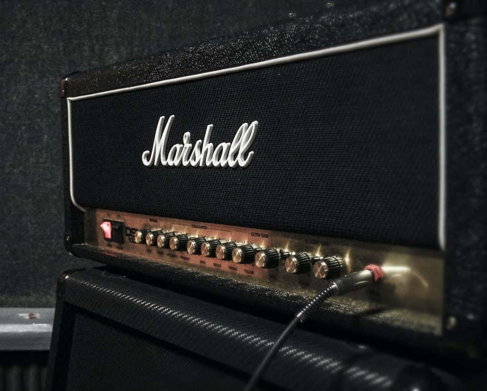 Guitar Amp 桌布 壁紙 — 復古黑色Marshall吉他音箱特寫，帶有發光旋鈕和紅色電源指示燈，背景為深色紋理牆壁。