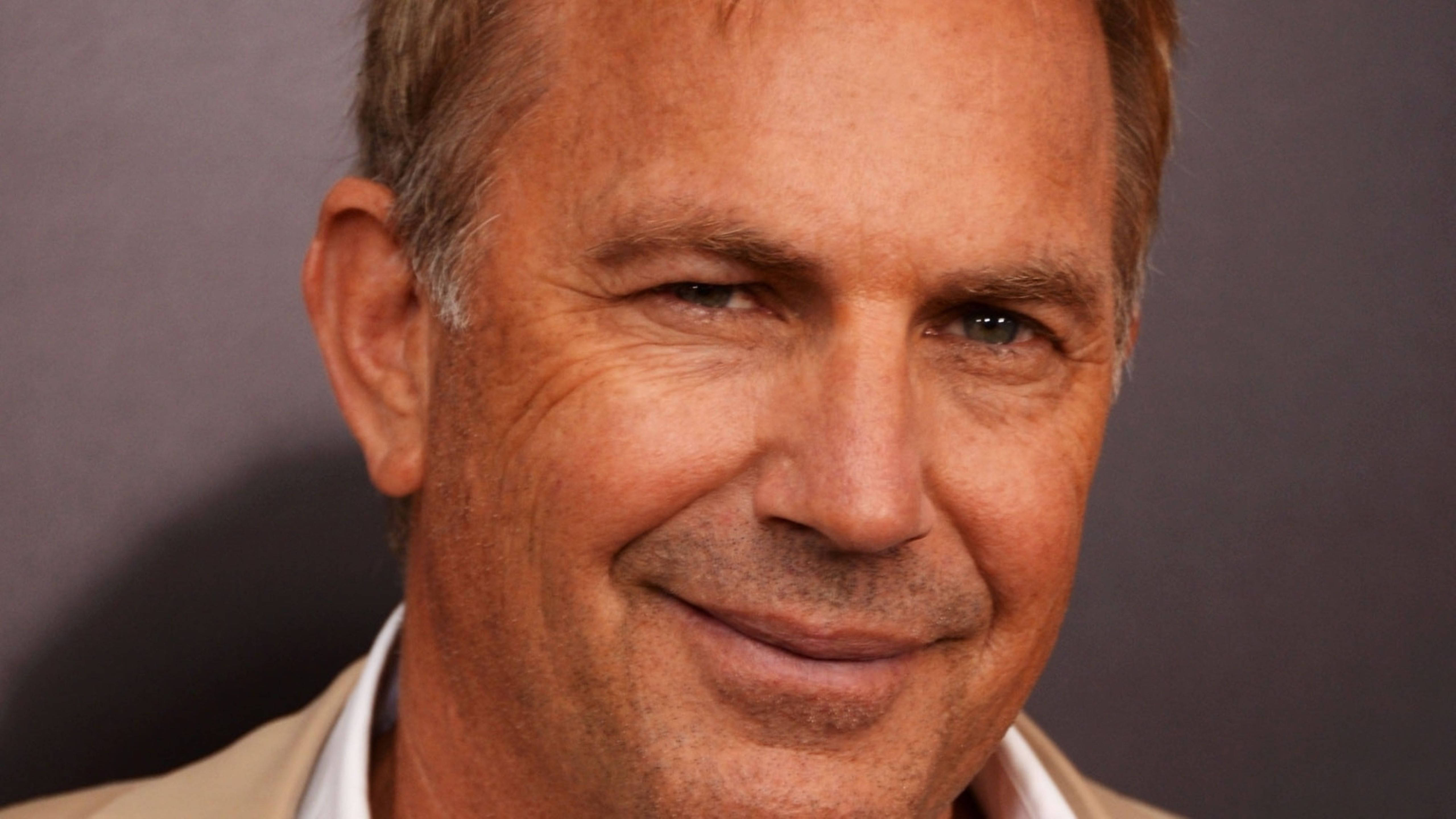 Kevin Costner 桌布 壁紙 — 微笑中年男士的特寫肖像，灰白頭髮，溫暖的眼神，背景為柔和的灰色。