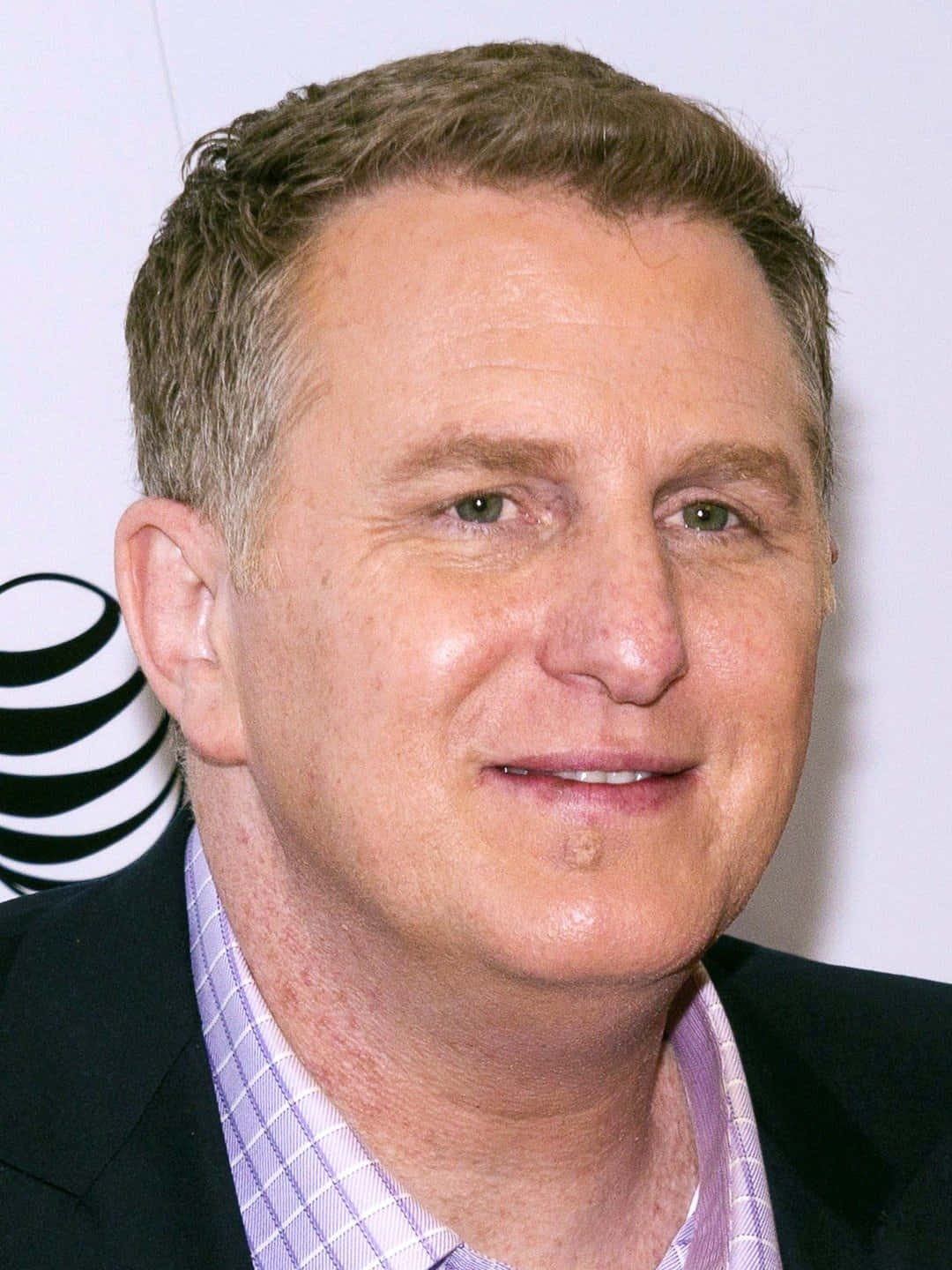 Michael Rapaport 桌布 壁紙 — 微笑中年短棕髮男士的特寫肖像，身穿深色西裝和淺紫色格紋襯衫。