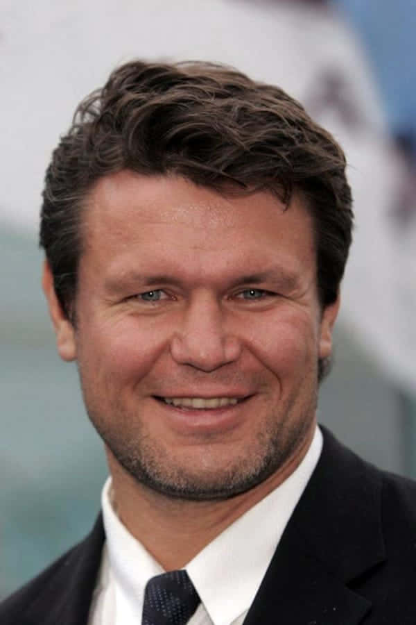 Celebrity 桌布 壁紙 — 微笑男士的頭肩近照，深色頭髮、鬍渣，身穿西裝打領帶，背景模糊。