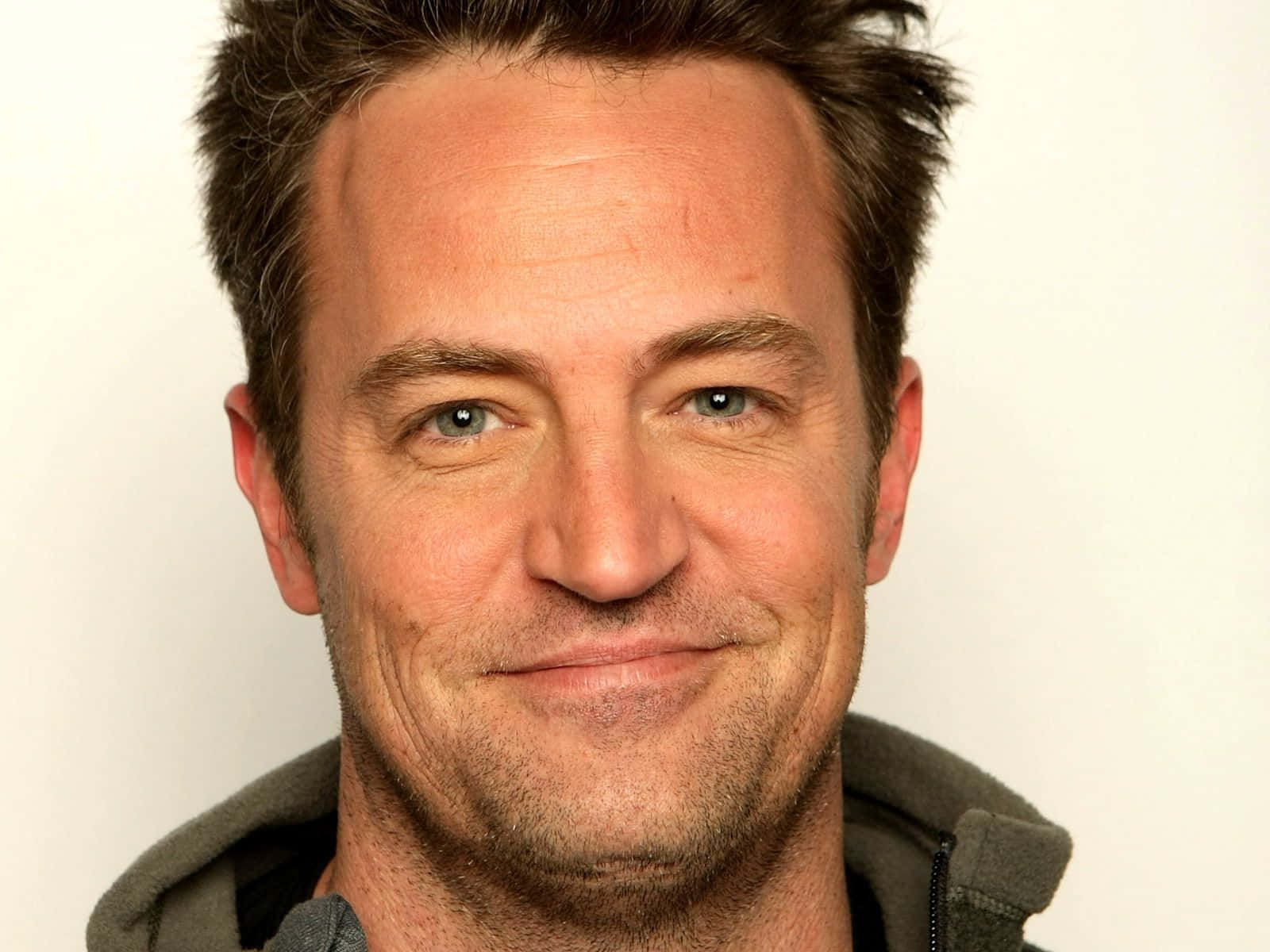 matthew perry 桌布 壁紙 — 微笑男子藍眼睛鬍渣特寫肖像，背景為純白色。