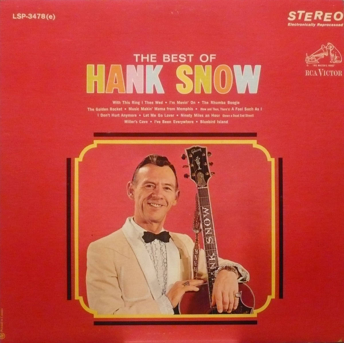 音樂 桌布 壁紙 — 微笑的Hank Snow身穿米色西裝和領結，在帶有金色邊框和歌曲名稱的醒目紅色專輯封面上拿著吉他。