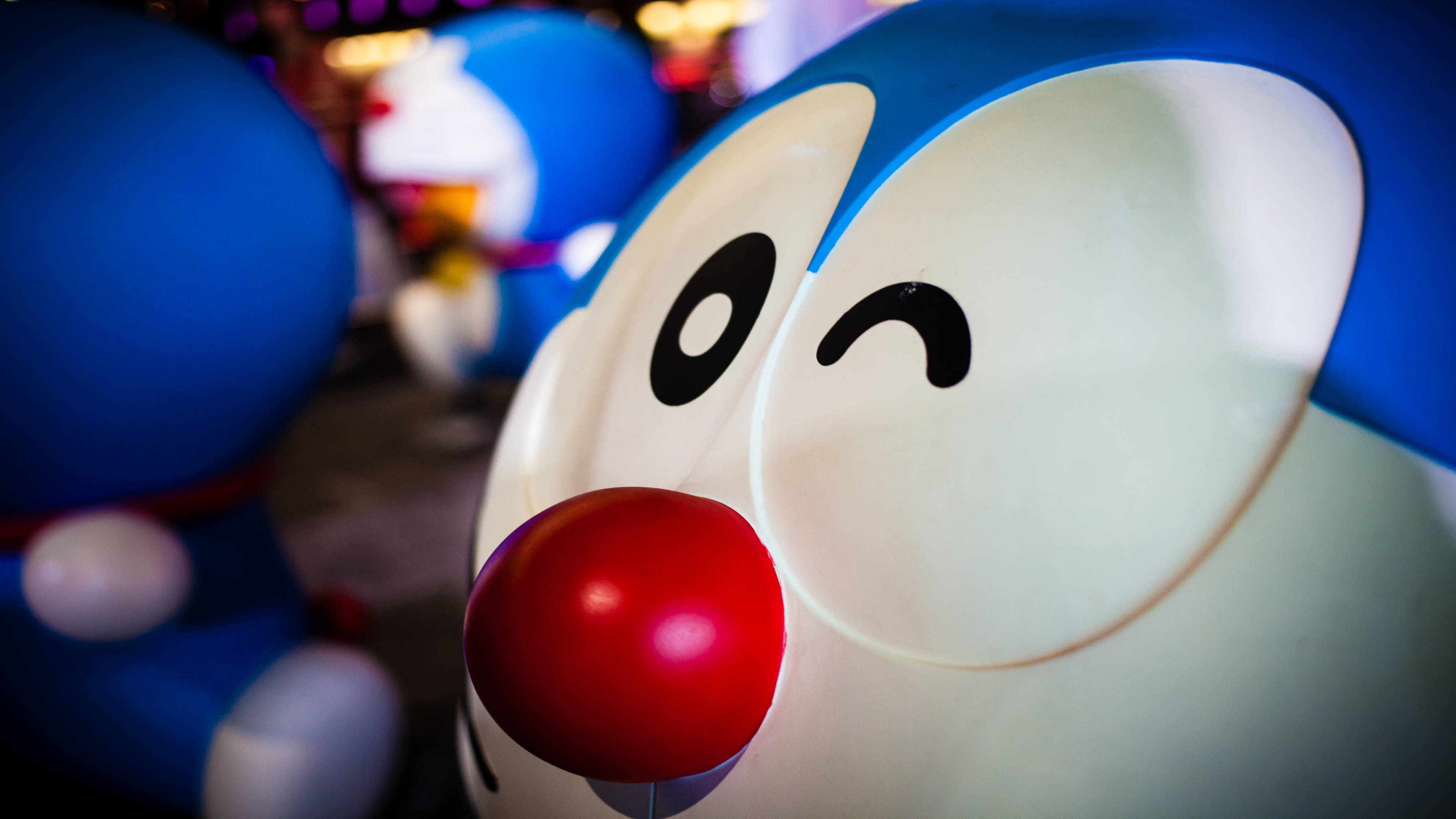 Doraemon 桌布 壁紙 — 微笑的哆啦A夢雕像特寫，紅色鼻子在夜間燈光下發光。