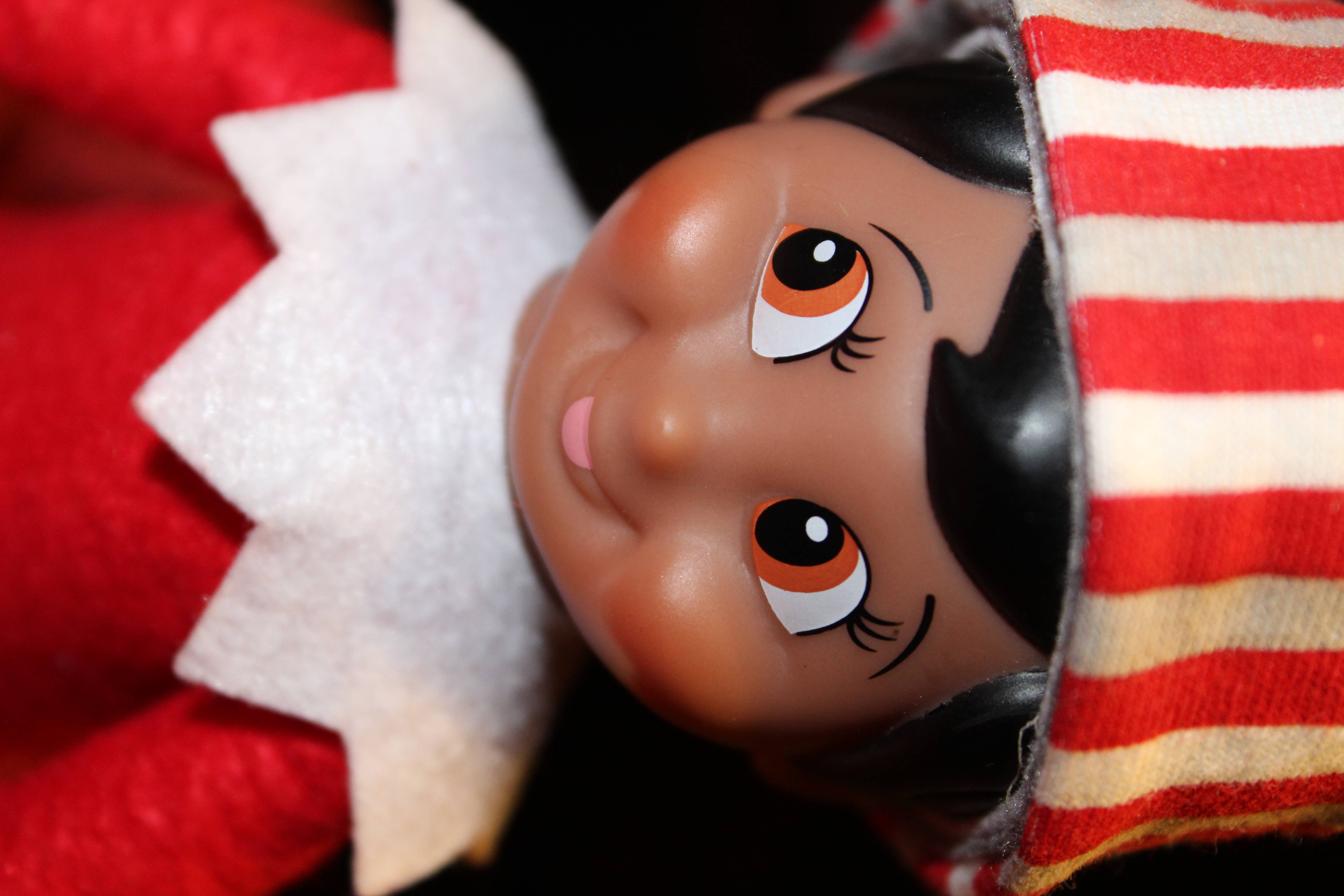 Christmas Elf 桌布 壁紙 — 微笑的精靈娃娃特寫，擁有橙色大眼睛，戴著紅白條紋帽子和紅色服裝。