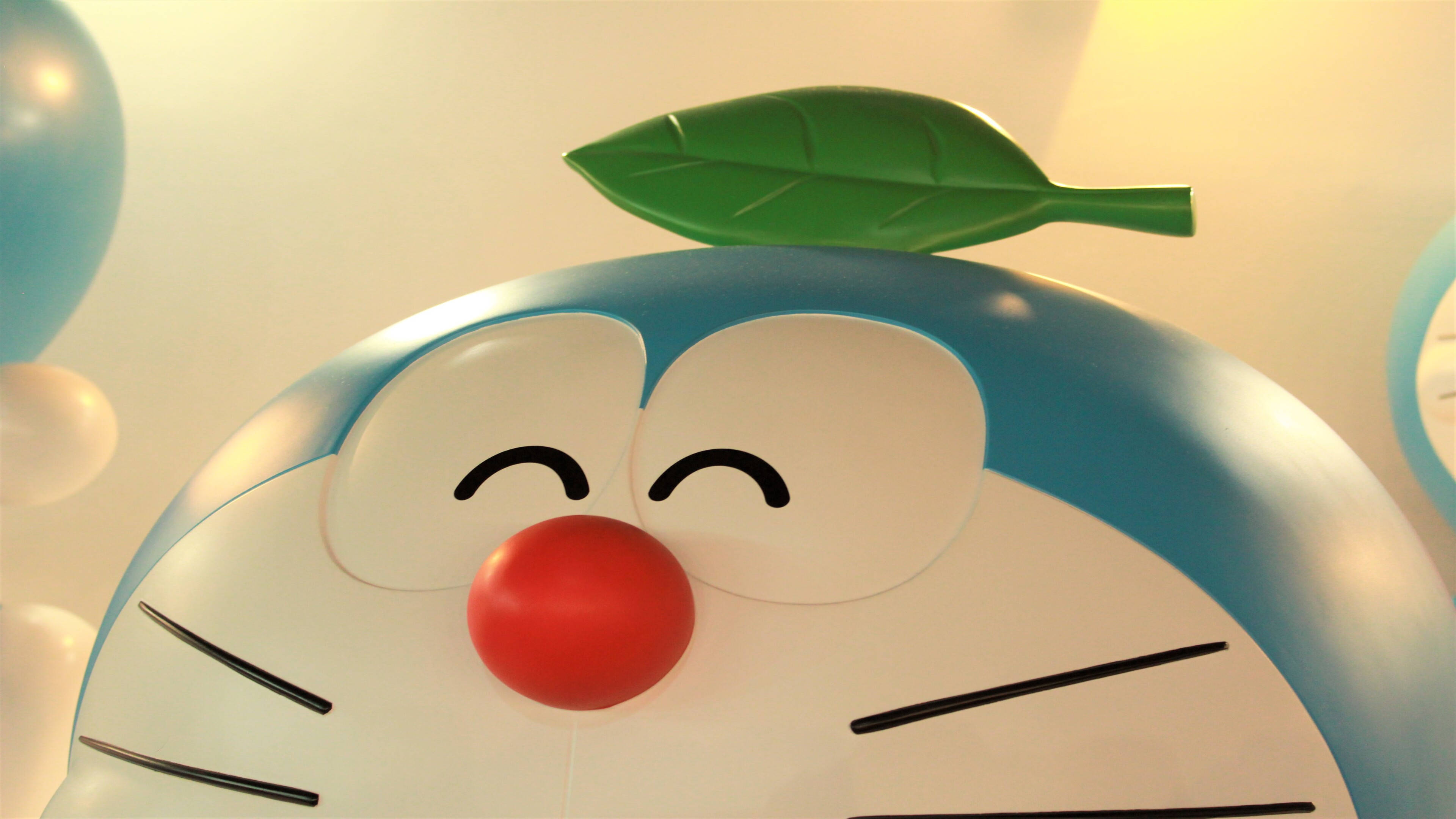 Doraemon 桌布 壁紙 — 微笑的藍色機器貓特寫，頭上一片綠葉，柔和溫暖的燈光。
