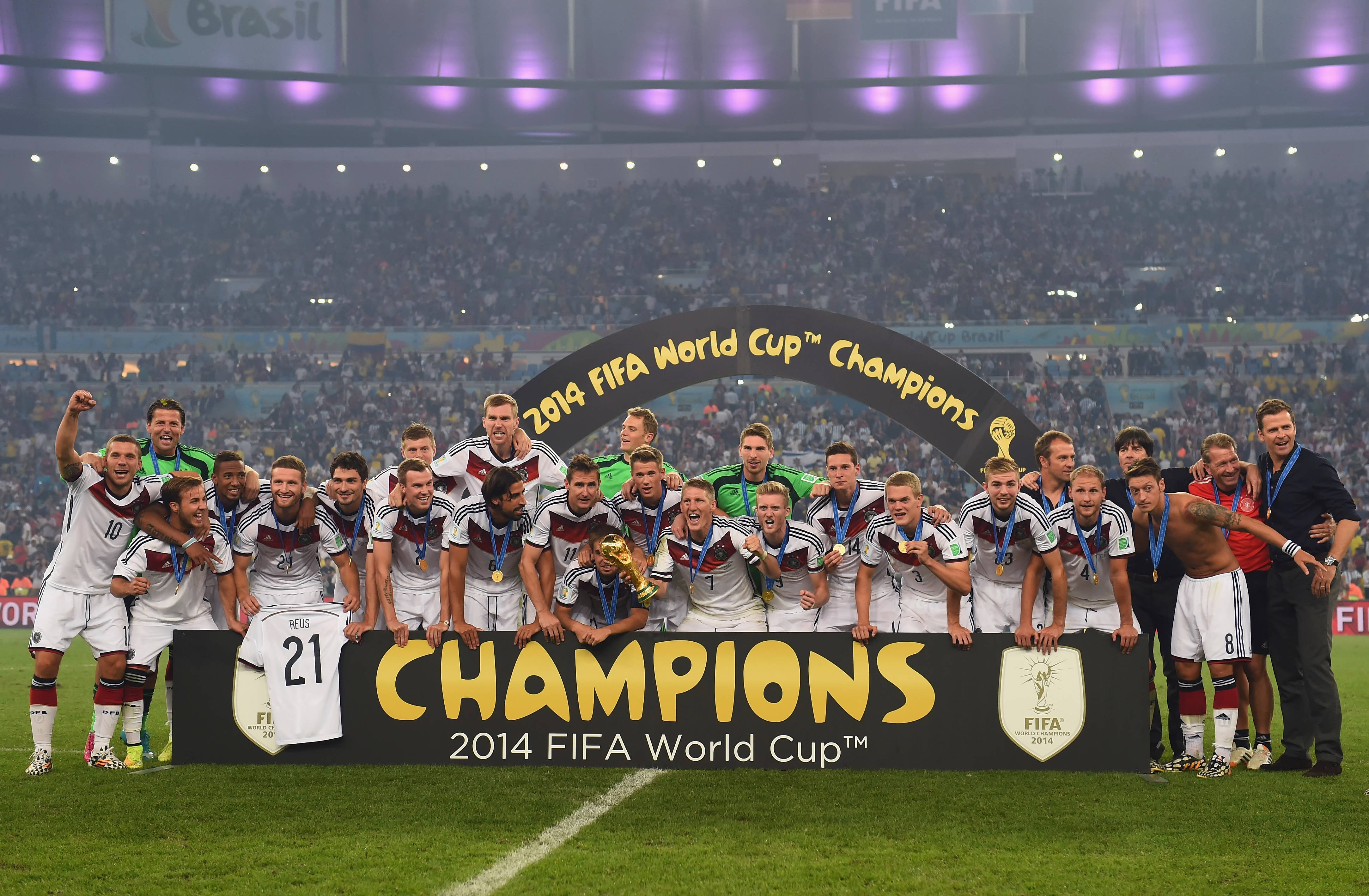World 桌布 壁紙 — 德國足球隊在球場燈光下高舉獎盃慶祝勝利，並有「Champions」橫幅。