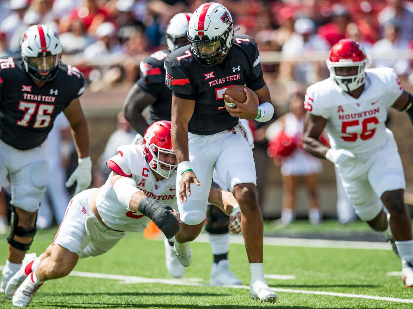 Texas Tech 桌布 壁紙 — 德州理工四分衛5號帶球奔跑，休士頓防守球員飛身擒抱，一場明亮的日間美式足球比賽。